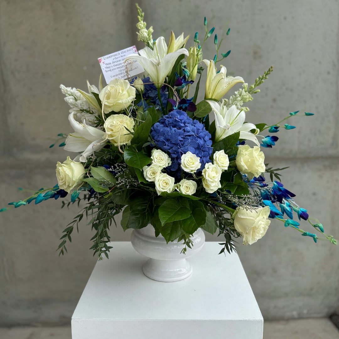 White lilies and roses with a blue hydrangea centerpiece in a white urn