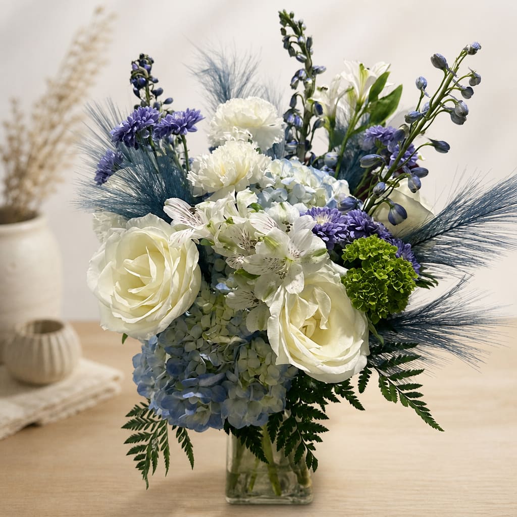 White roses and blue-purple flowers in a clear glass vase