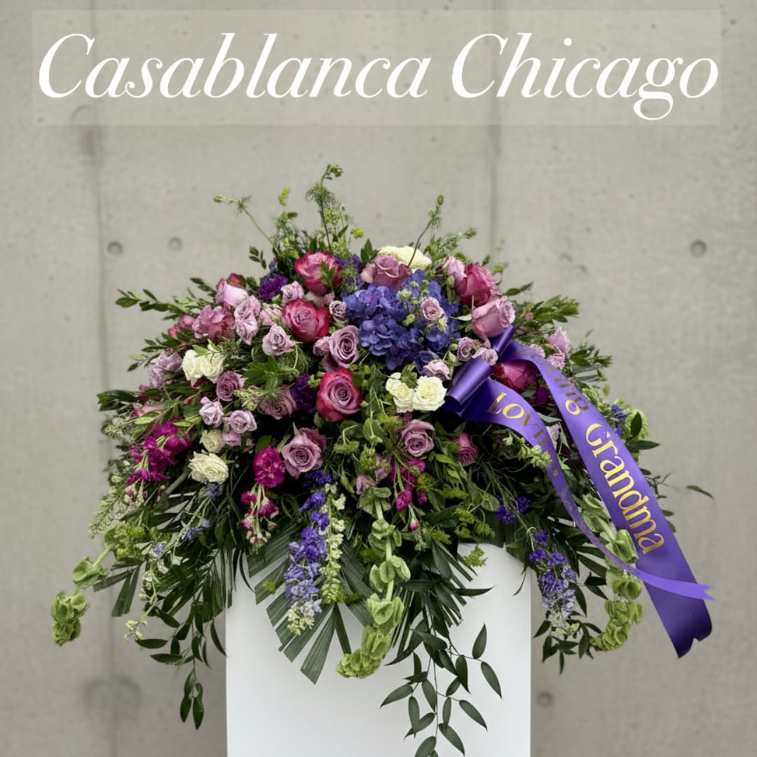 Large purple and pink floral arrangement in a white container with a ribbon