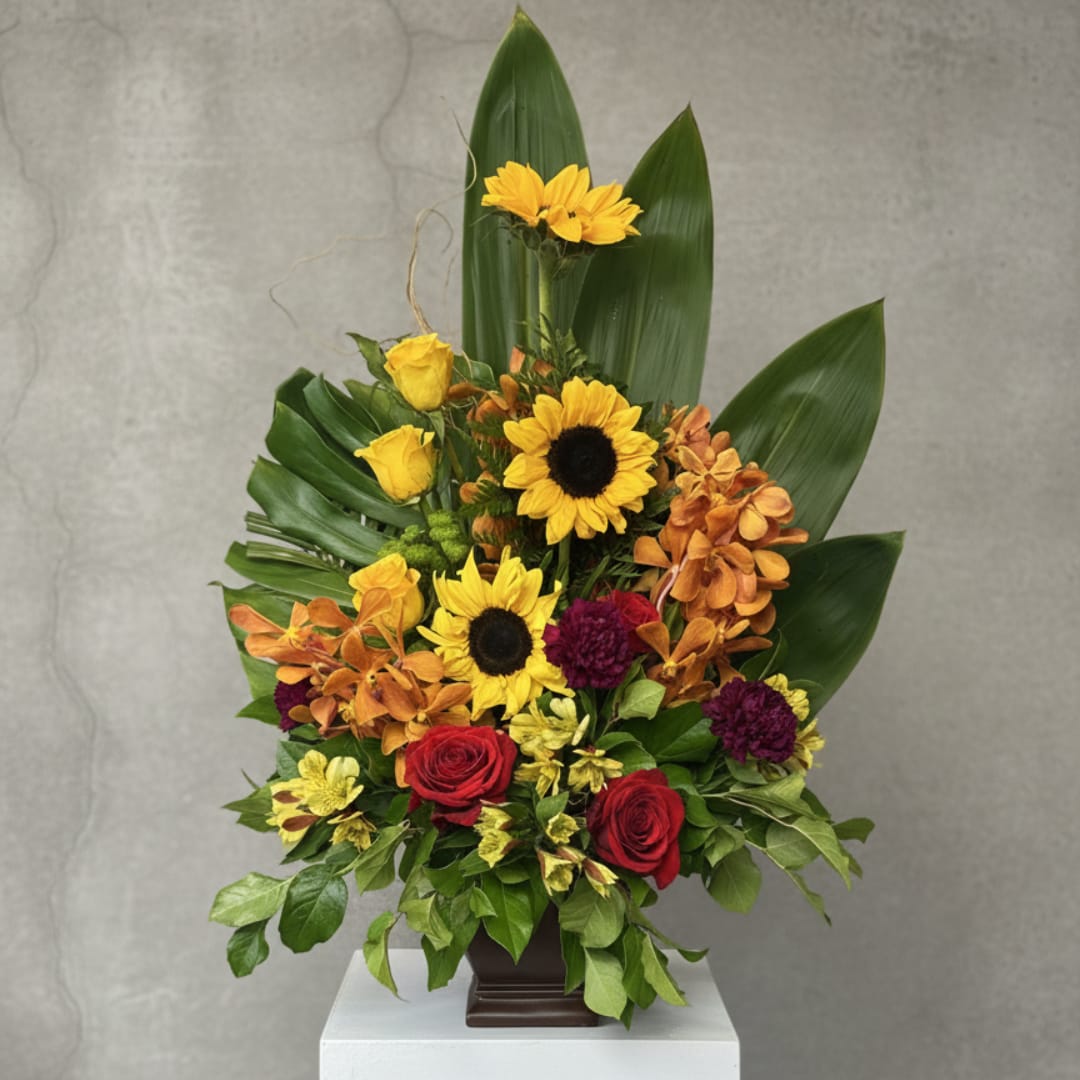 Mixed bouquet with sunflowers, red roses, and orange orchids in a dark vase