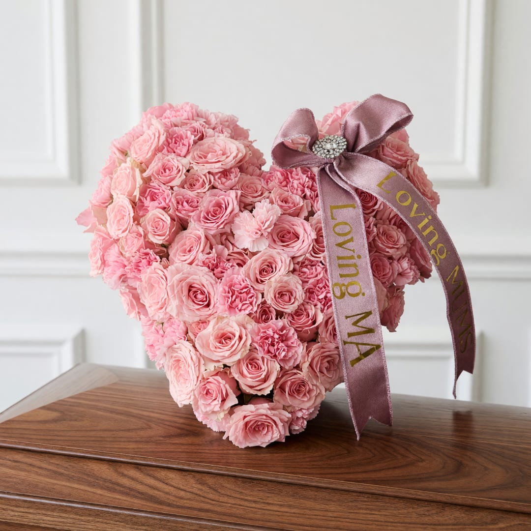 Heart-shaped pink rose arrangement with a satin ribbon on a wooden table