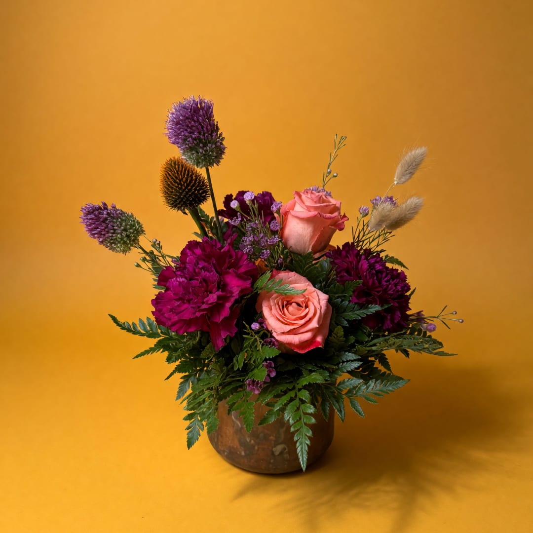Pink roses and magenta flowers arranged in a brown vase