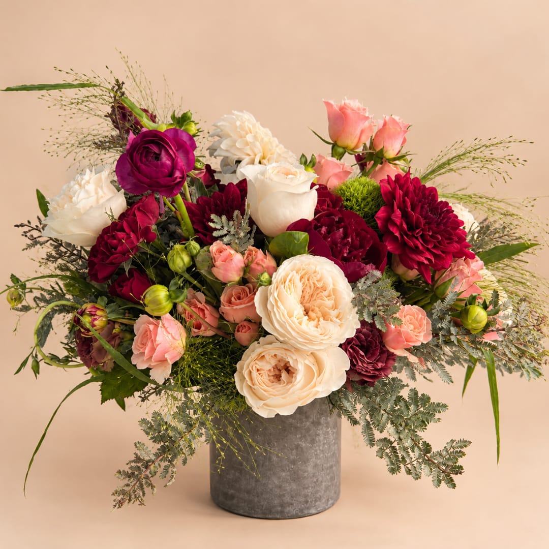 Mixed bouquet of cream, pink, and burgundy flowers in a gray vase