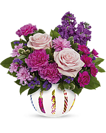 Pink and purple flower arrangement in a white vase with candle designs