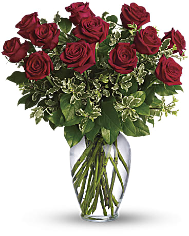 Red roses arranged in a clear glass vase with mixed greenery