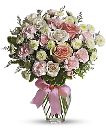 Pink and white rose bouquet in a clear glass vase with a pink ribbon