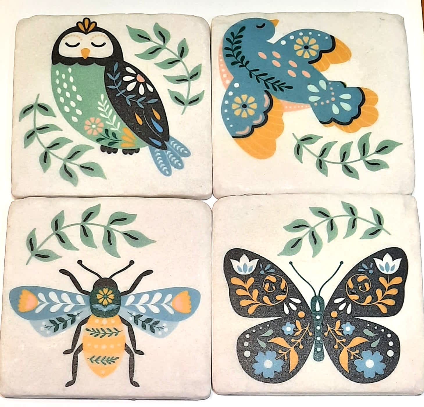 Four decorative tiles with stylized owl, bird, bee, and butterfly designs
