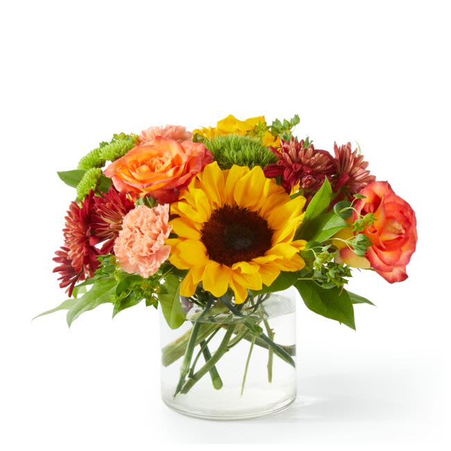 Mixed bouquet with a sunflower, roses, and carnations in a clear glass vase