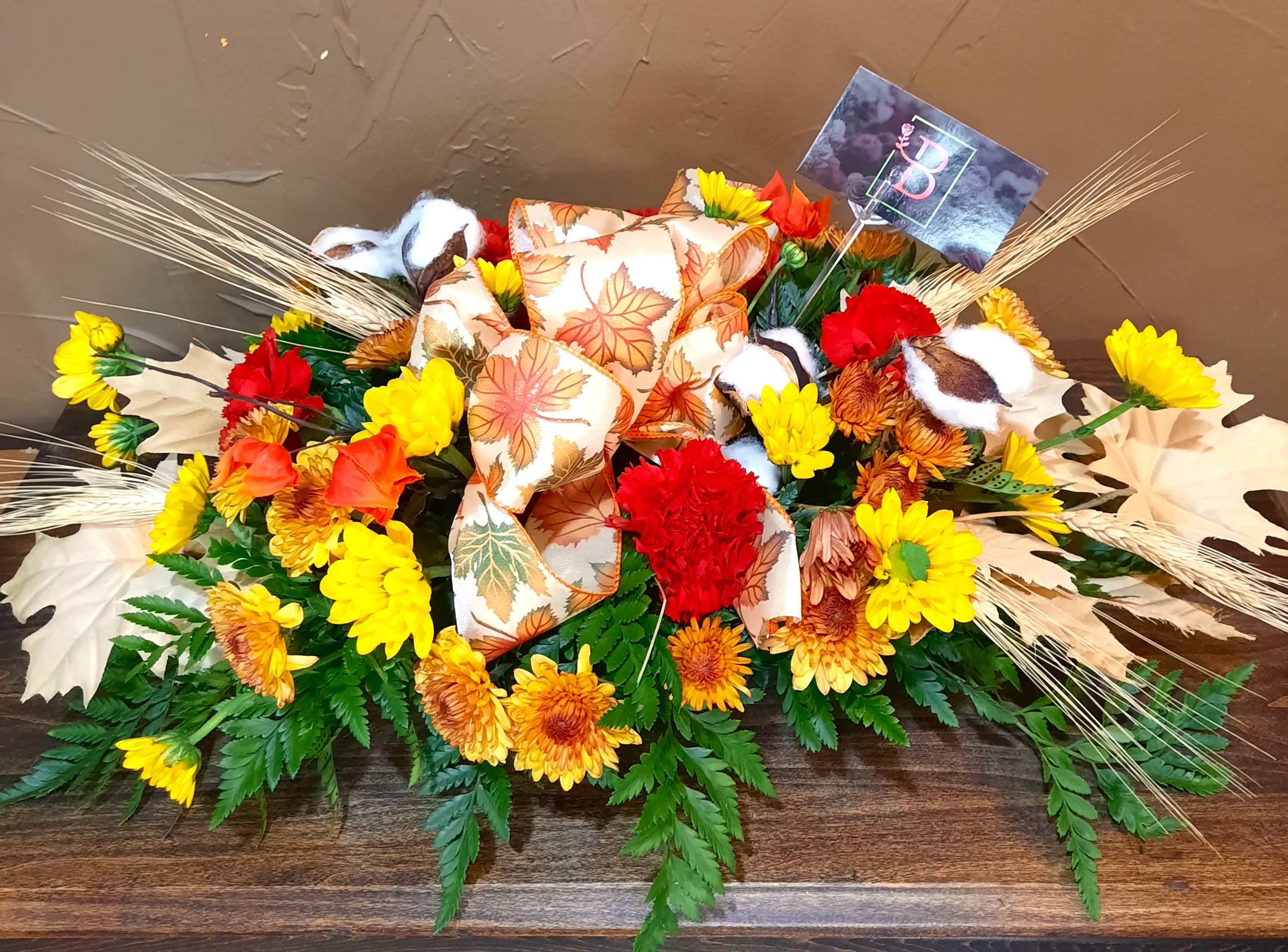 Autumn floral arrangement with yellow and red flowers and a leaf-patterned bow