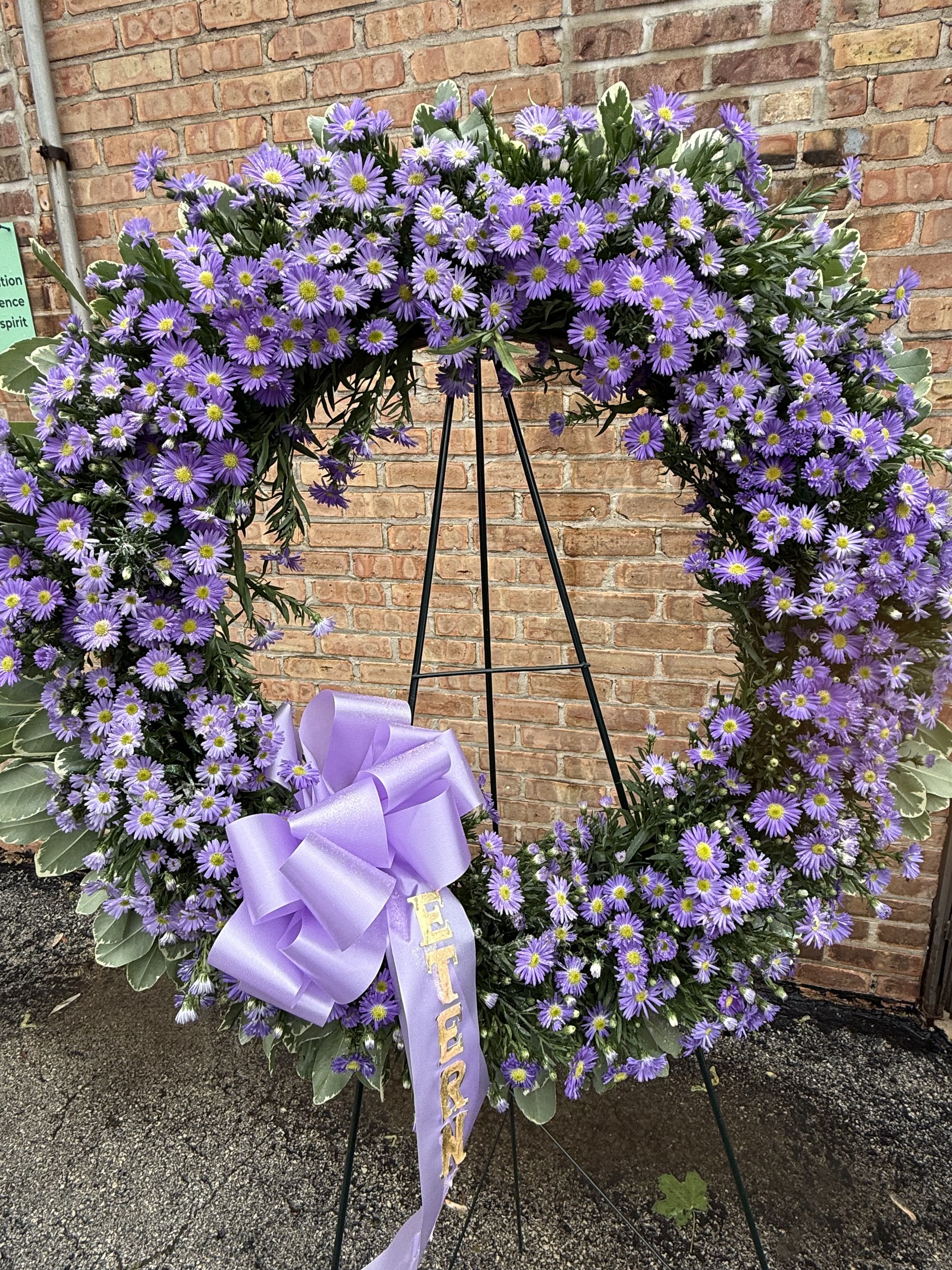 Purple daisy wreath on a black easel with a lavender ribbon bow