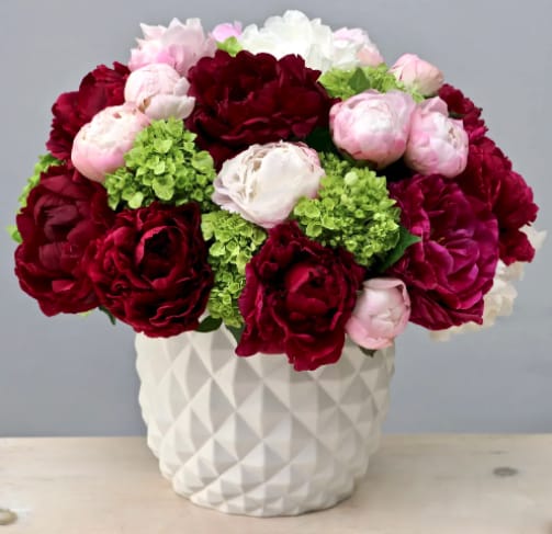 Red and pink peonies with green hydrangeas in a white vase