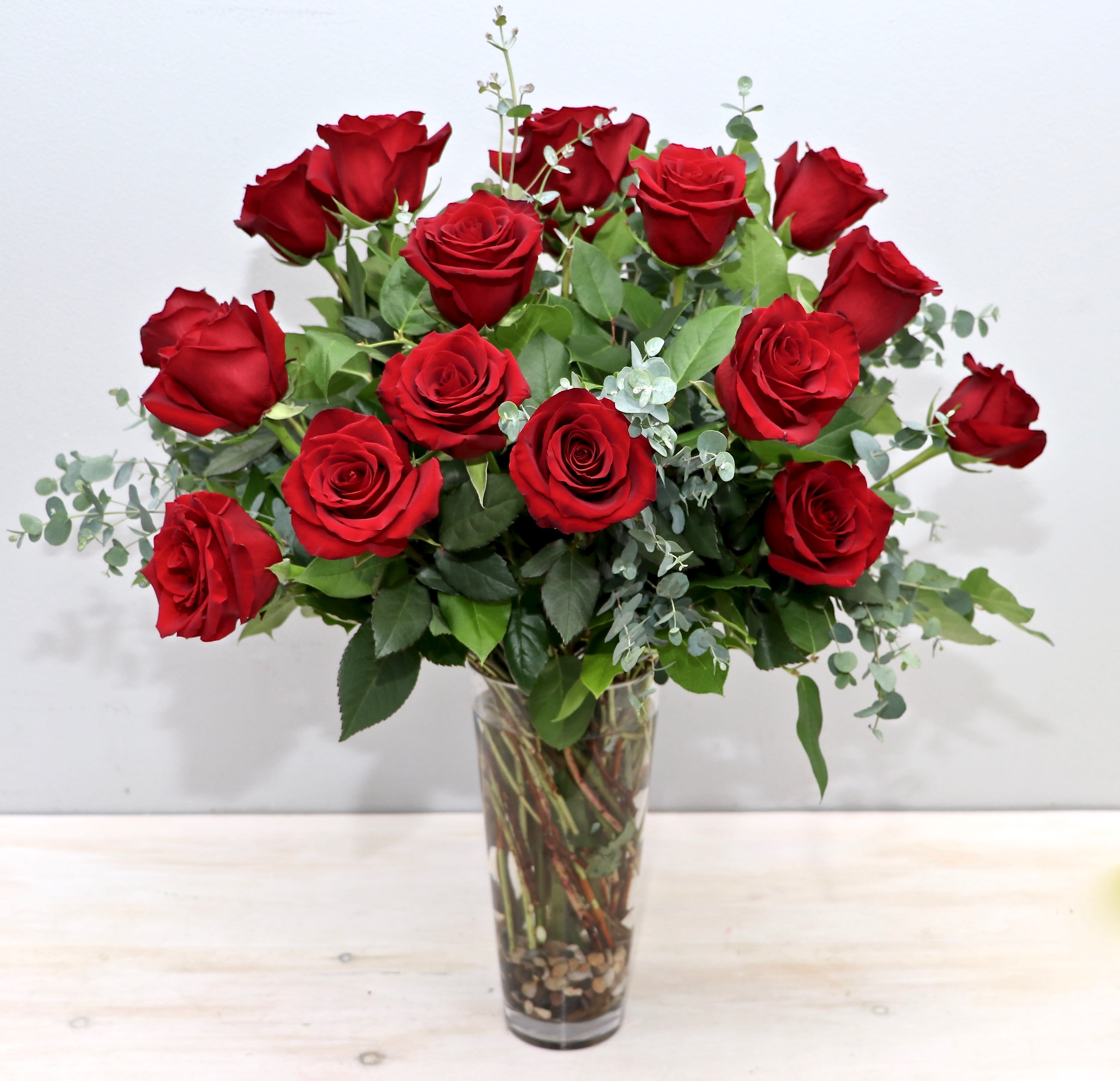 Tall arrangement of long-stem red roses in a clear glass vase with accent filler.