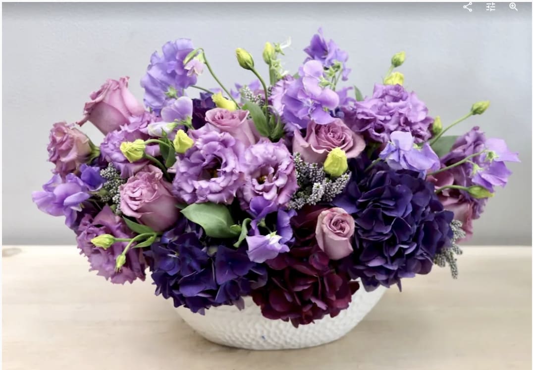 Purple and pink floral arrangement in a white bowl vase