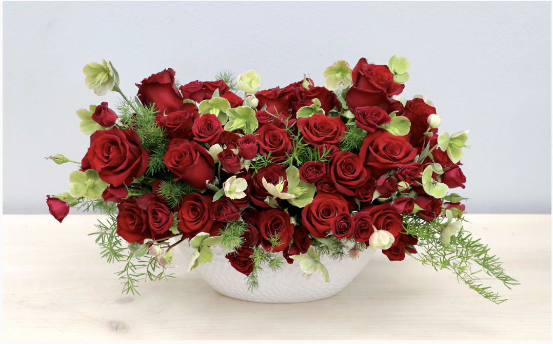 Red roses and pale green flowers in a white bowl vase