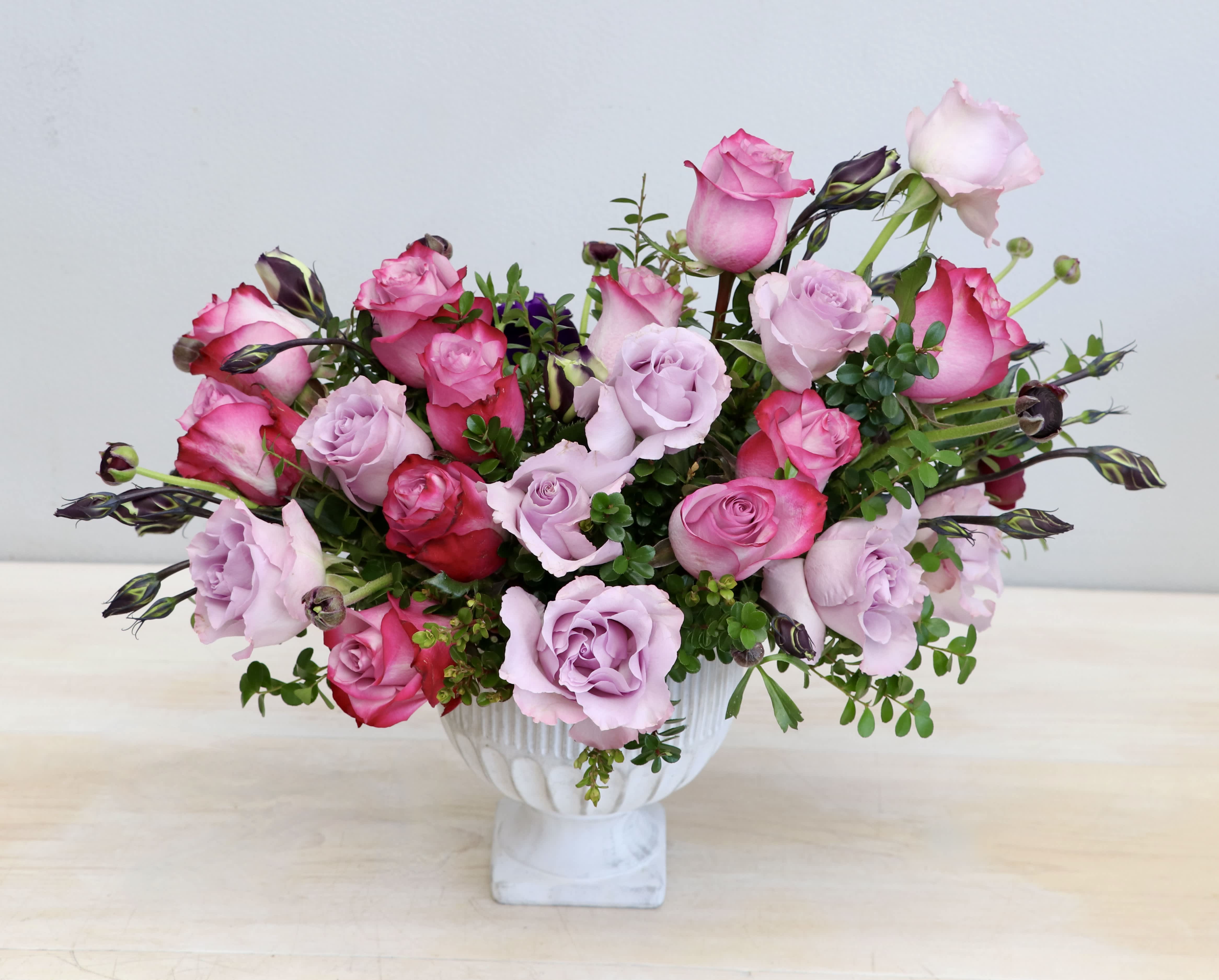 Pink and lavender roses arranged in a white pedestal vase