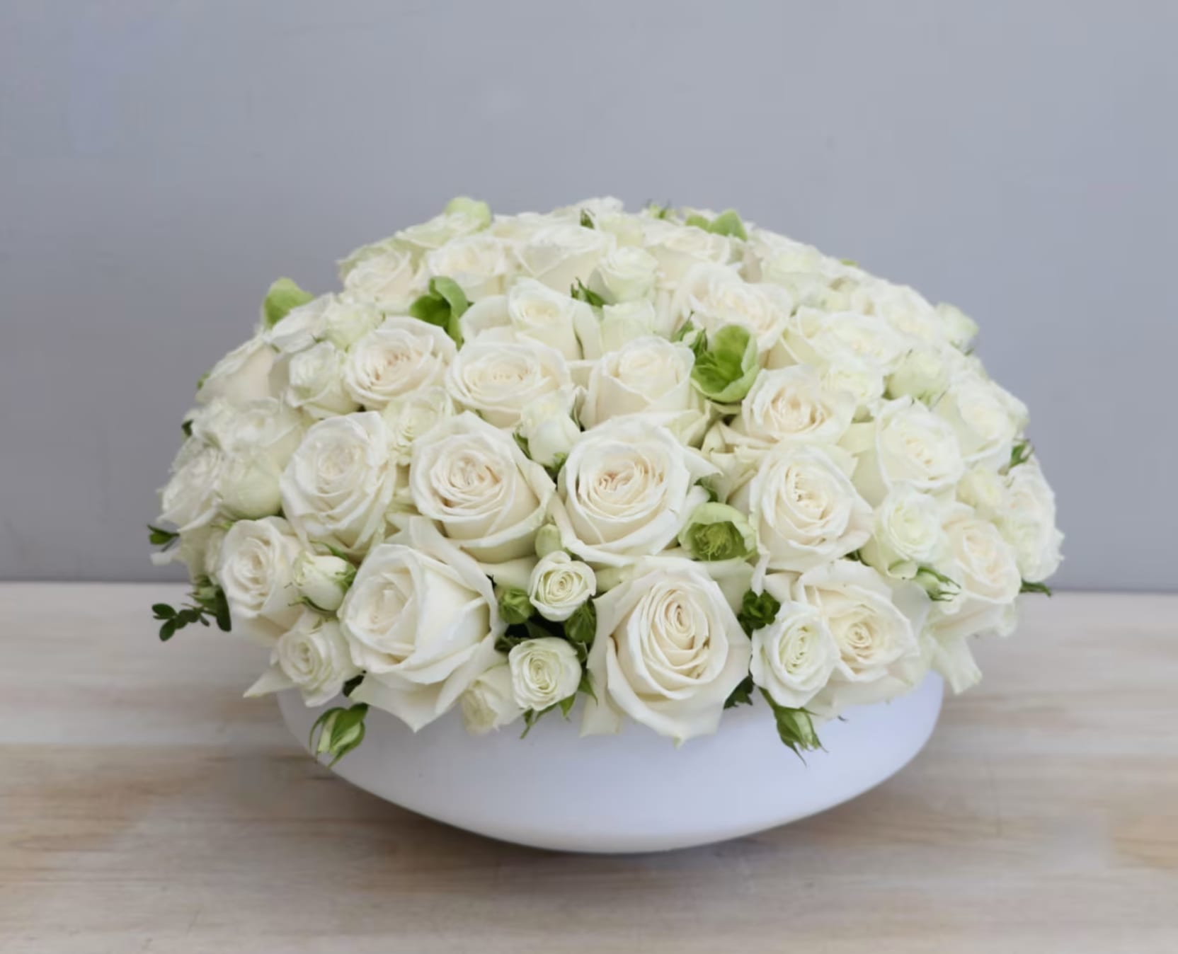 Low arrangement of cream and white roses tightly clustered in a round white bowl