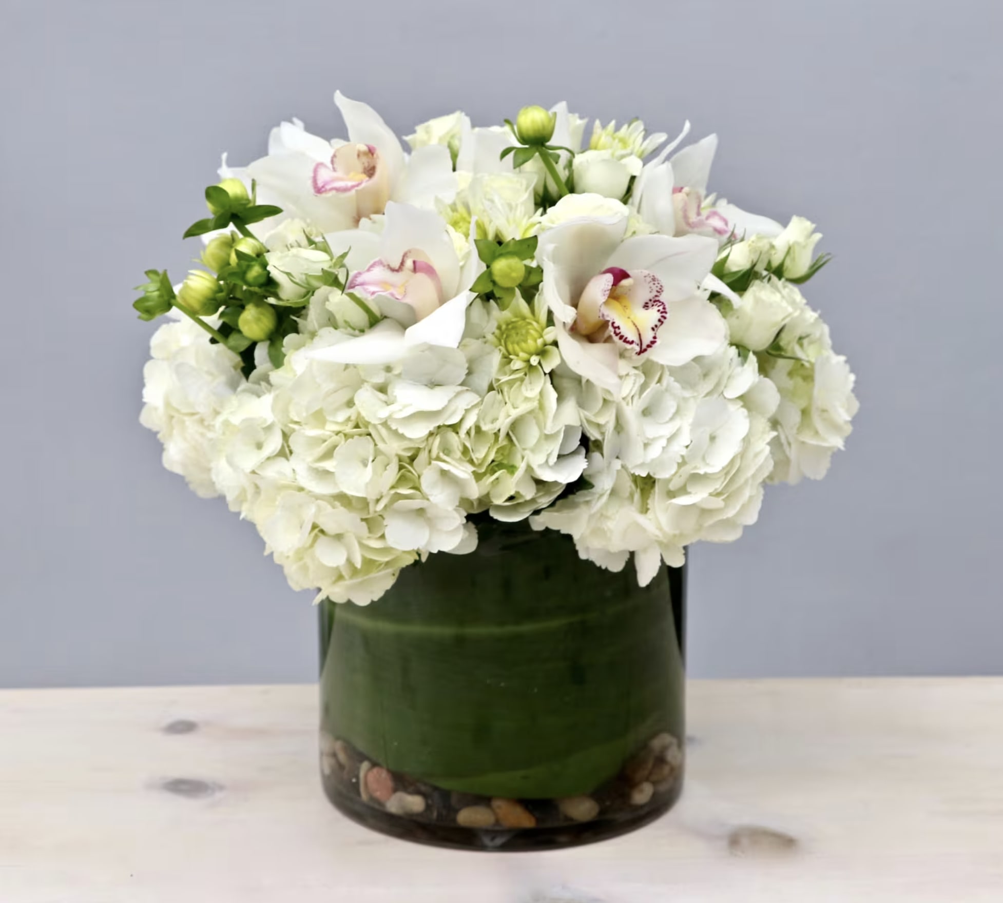 White hydrangeas and orchids arranged in a glass vase