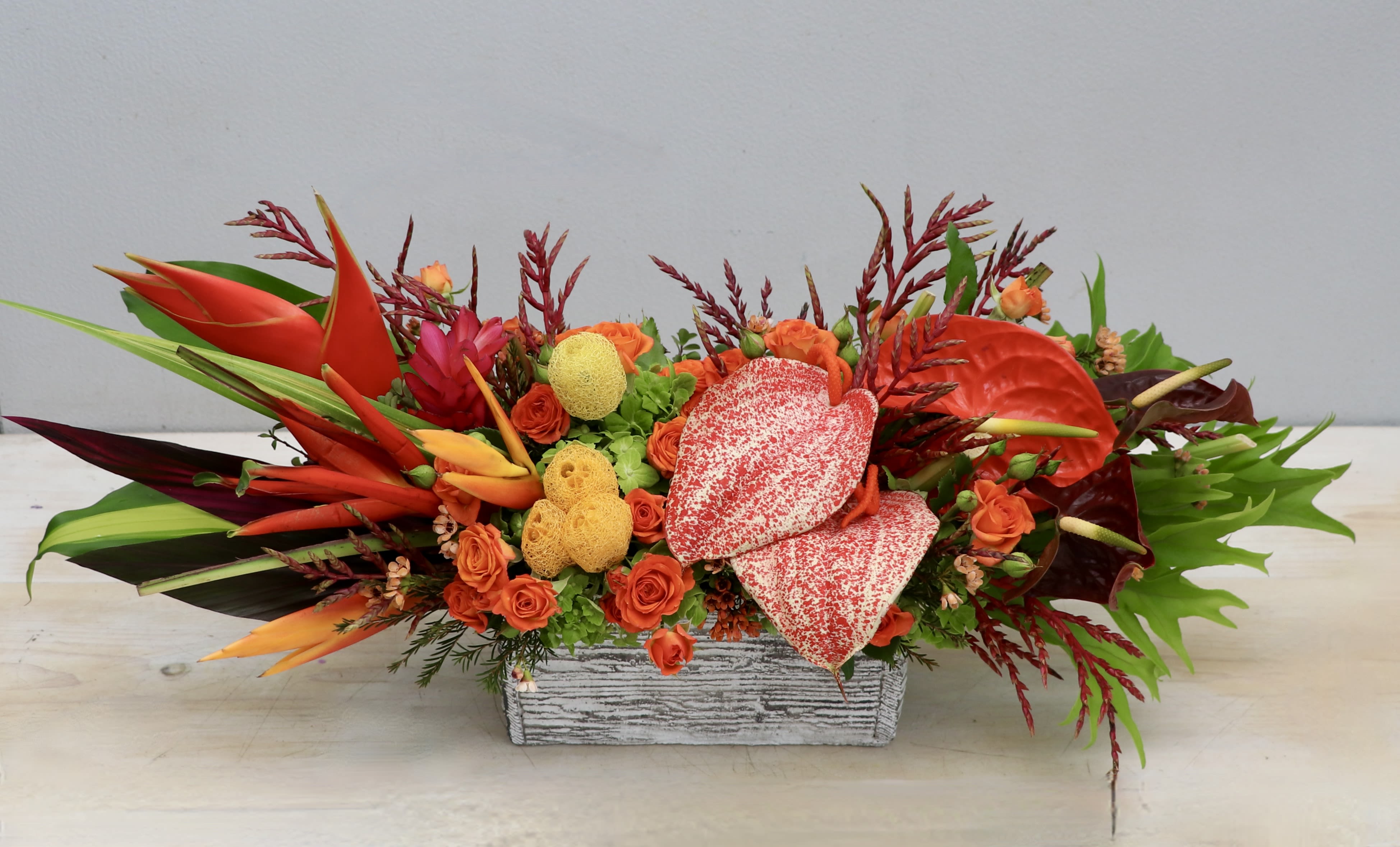 Tropical floral arrangement with orange and red blooms in a rectangular container