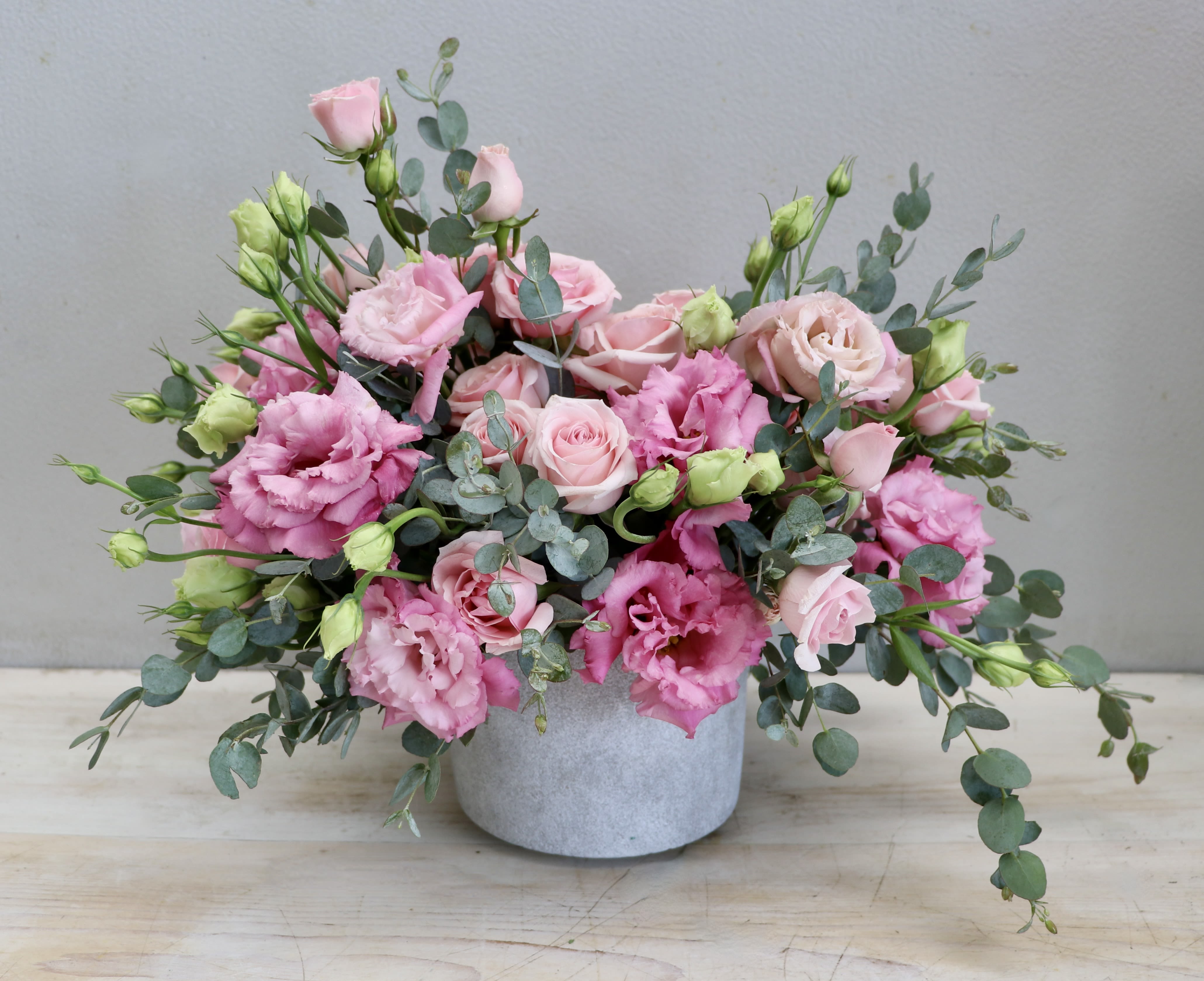 Pink roses and lisianthus in a gray vase with eucalyptus