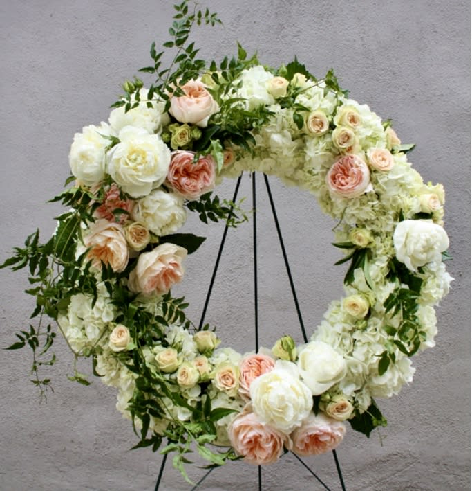 Floral wreath of white and peach roses on a black stand