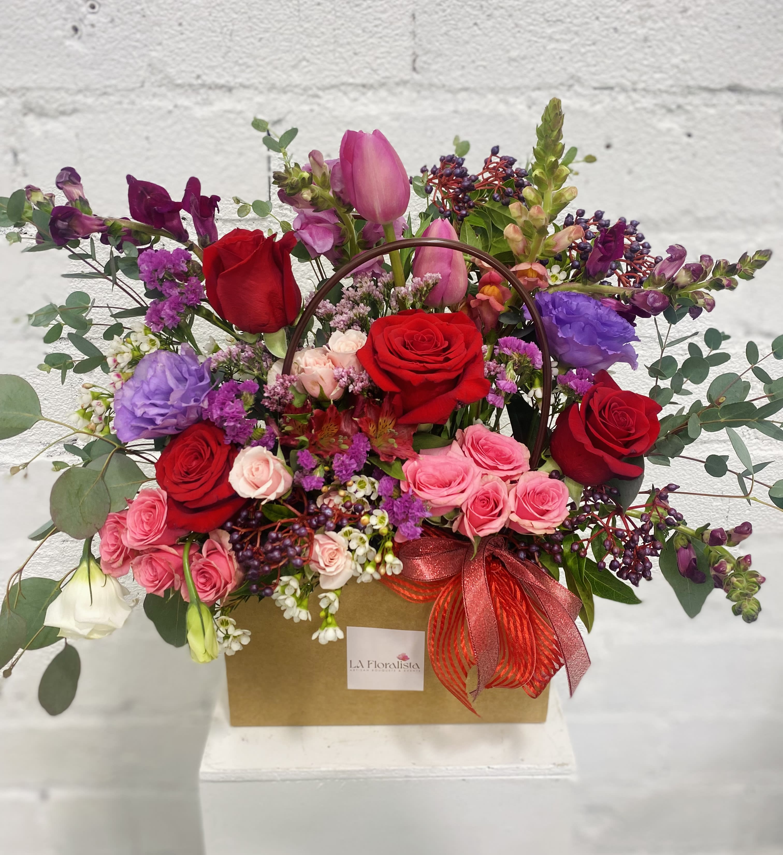 Mixed bouquet of roses, tulips, and purple blooms in a gift box with a ribbon