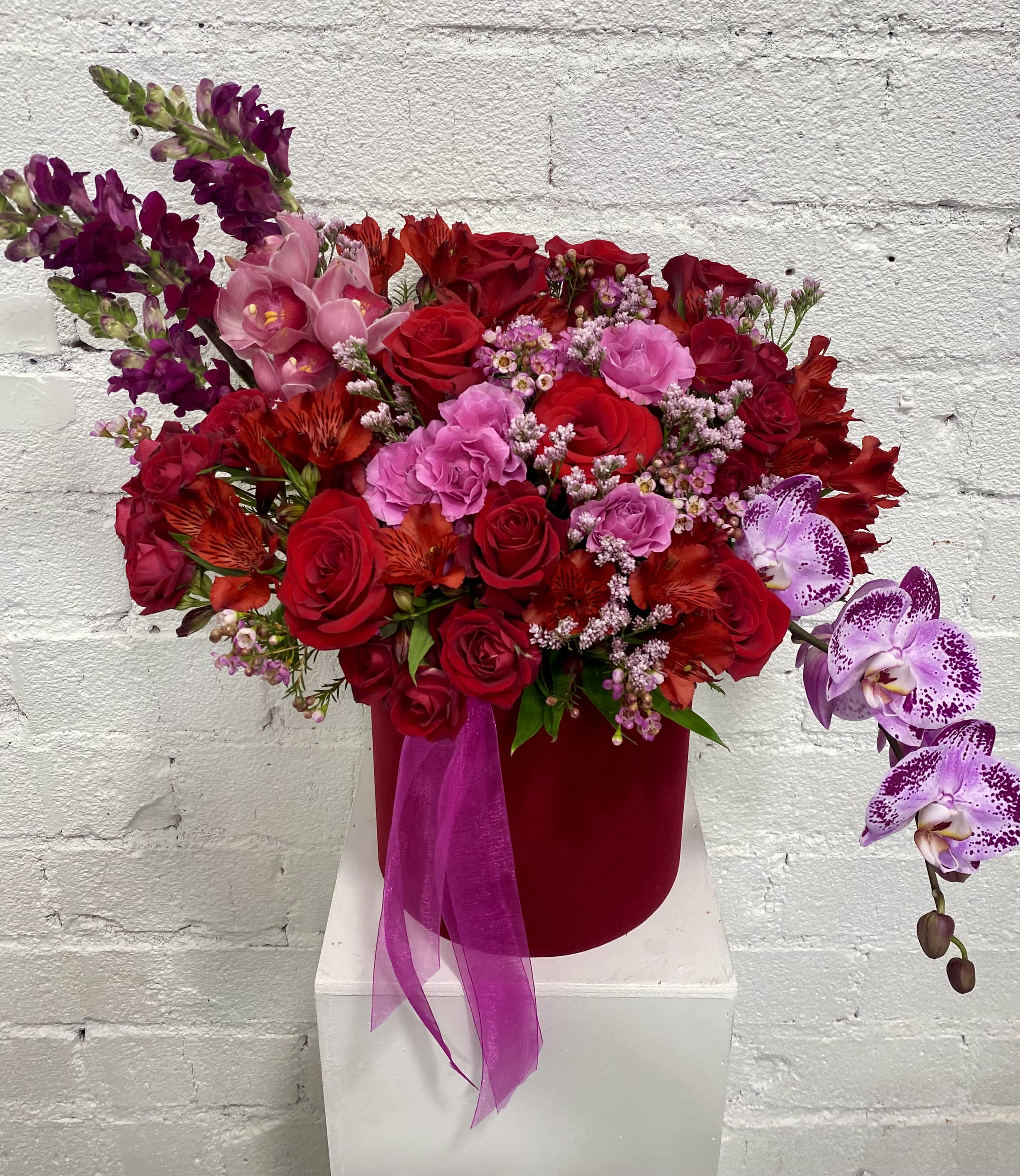 Red and pink floral arrangement in a velvet box with orchid sprays
