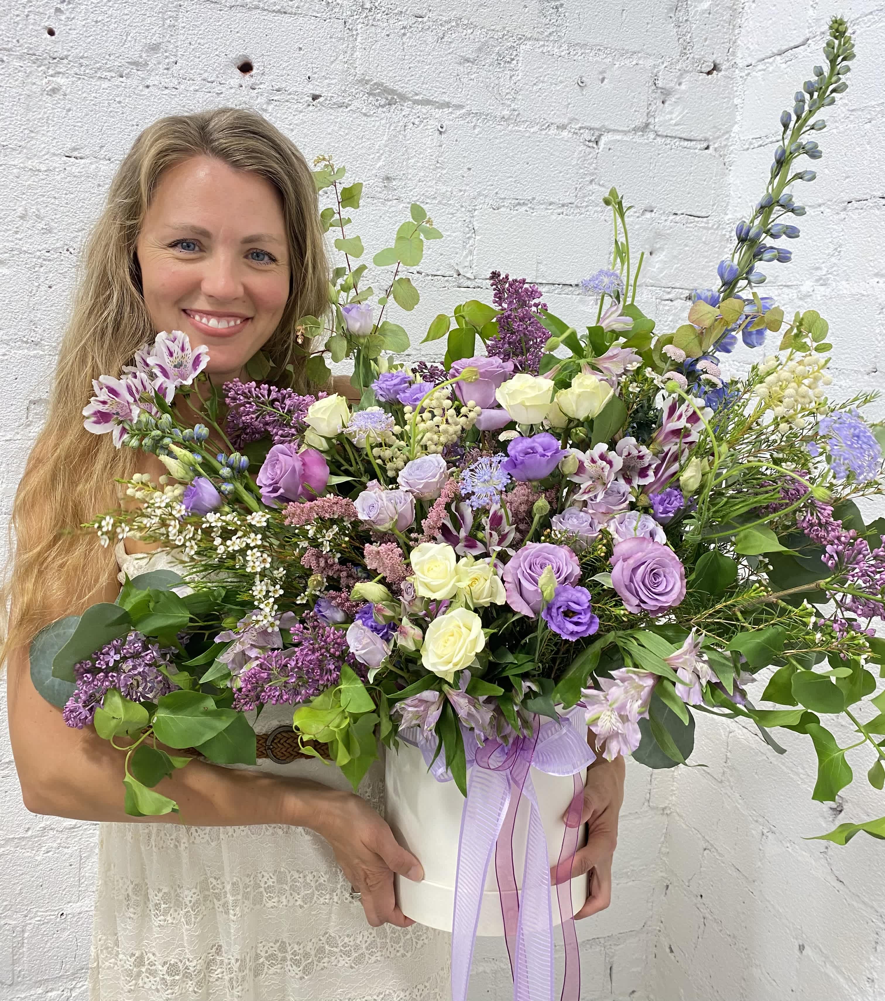 Woman holding a large lavender and white floral arrangement in a white box