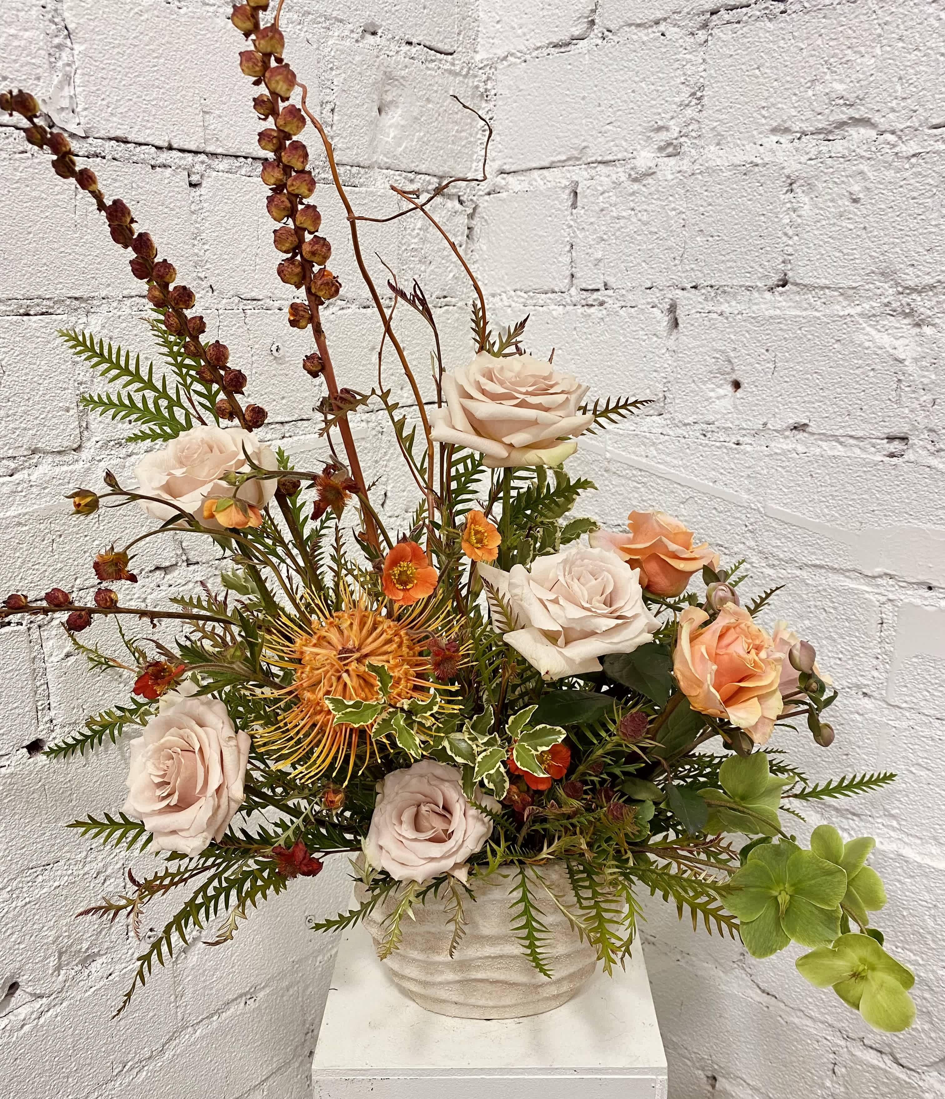 Mixed floral arrangement in a white vase with pale roses and orange blooms