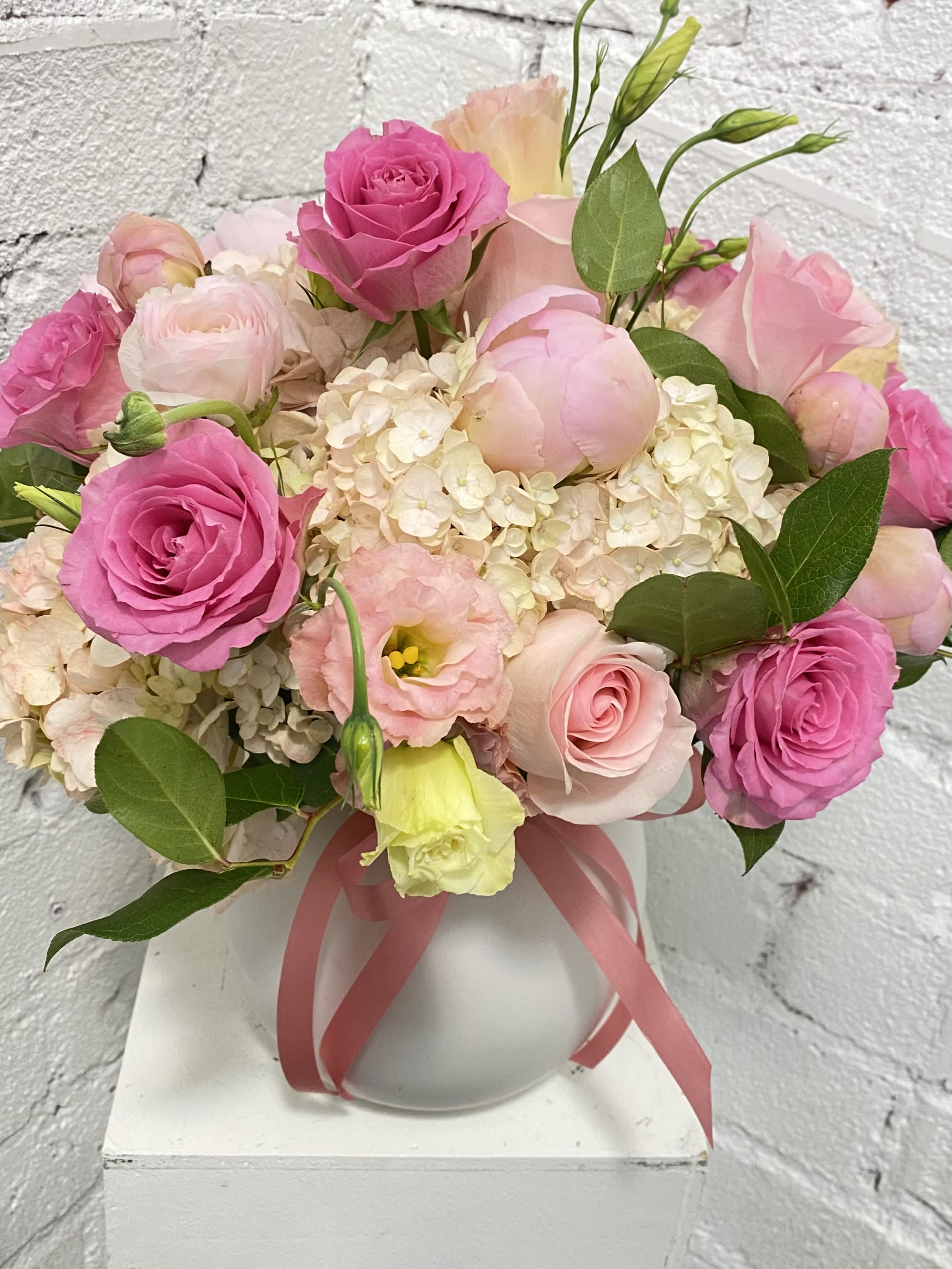Pink roses and pale blooms arranged in a white vase with a ribbon