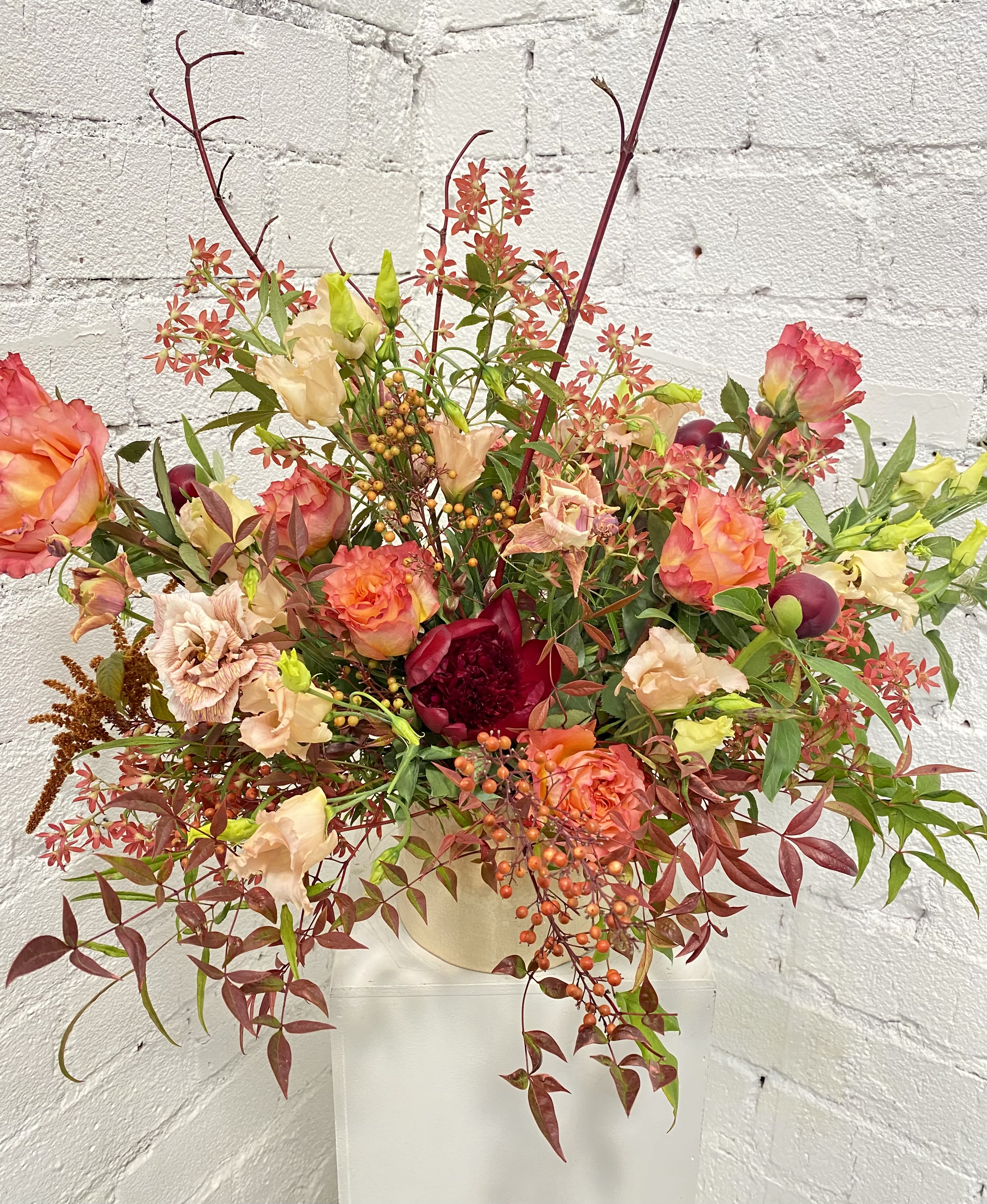 Large mixed floral arrangement in a cream vase with coral and peach blooms