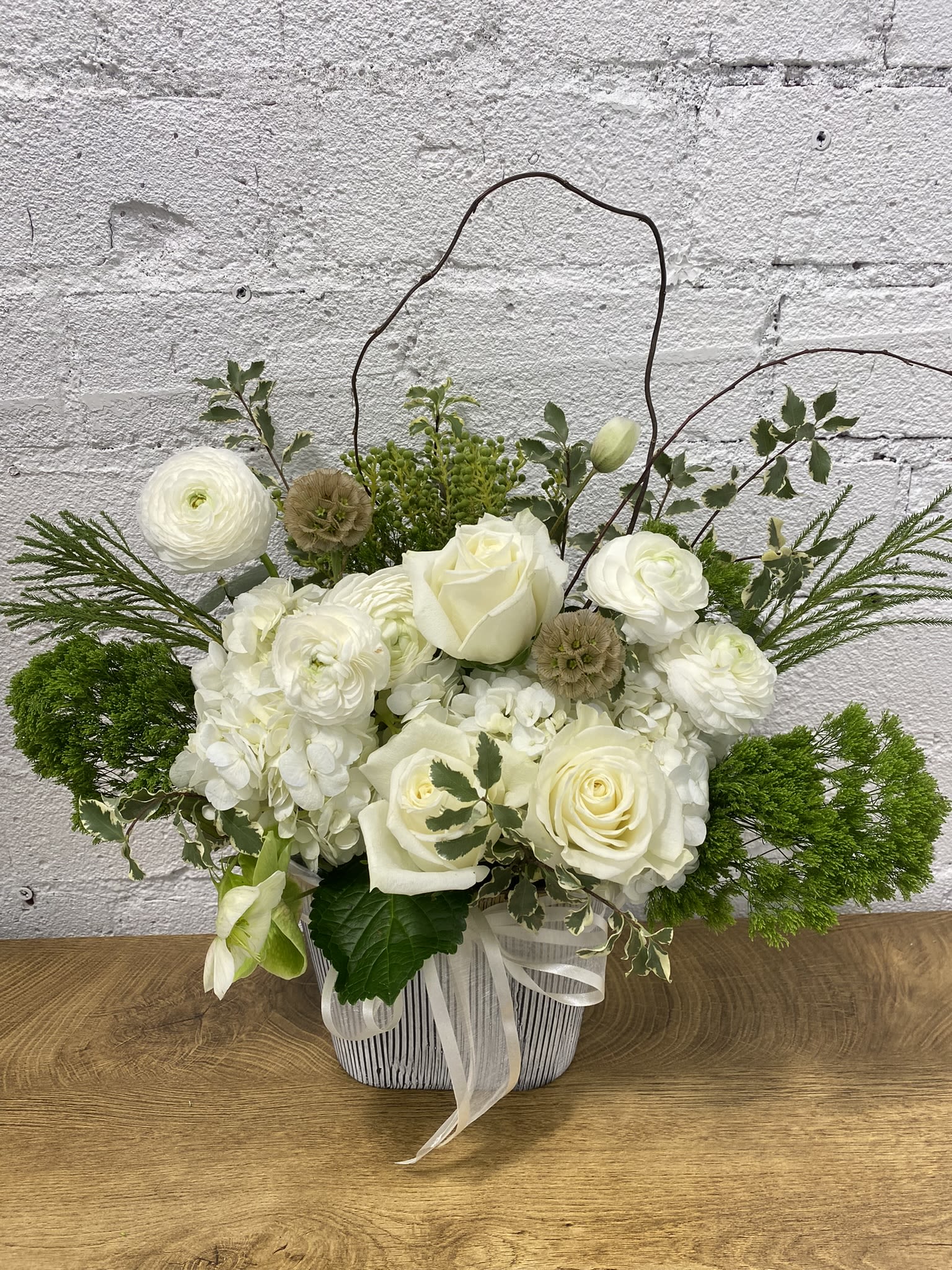 White roses and ranunculus in a striped basket with a ribbon handle