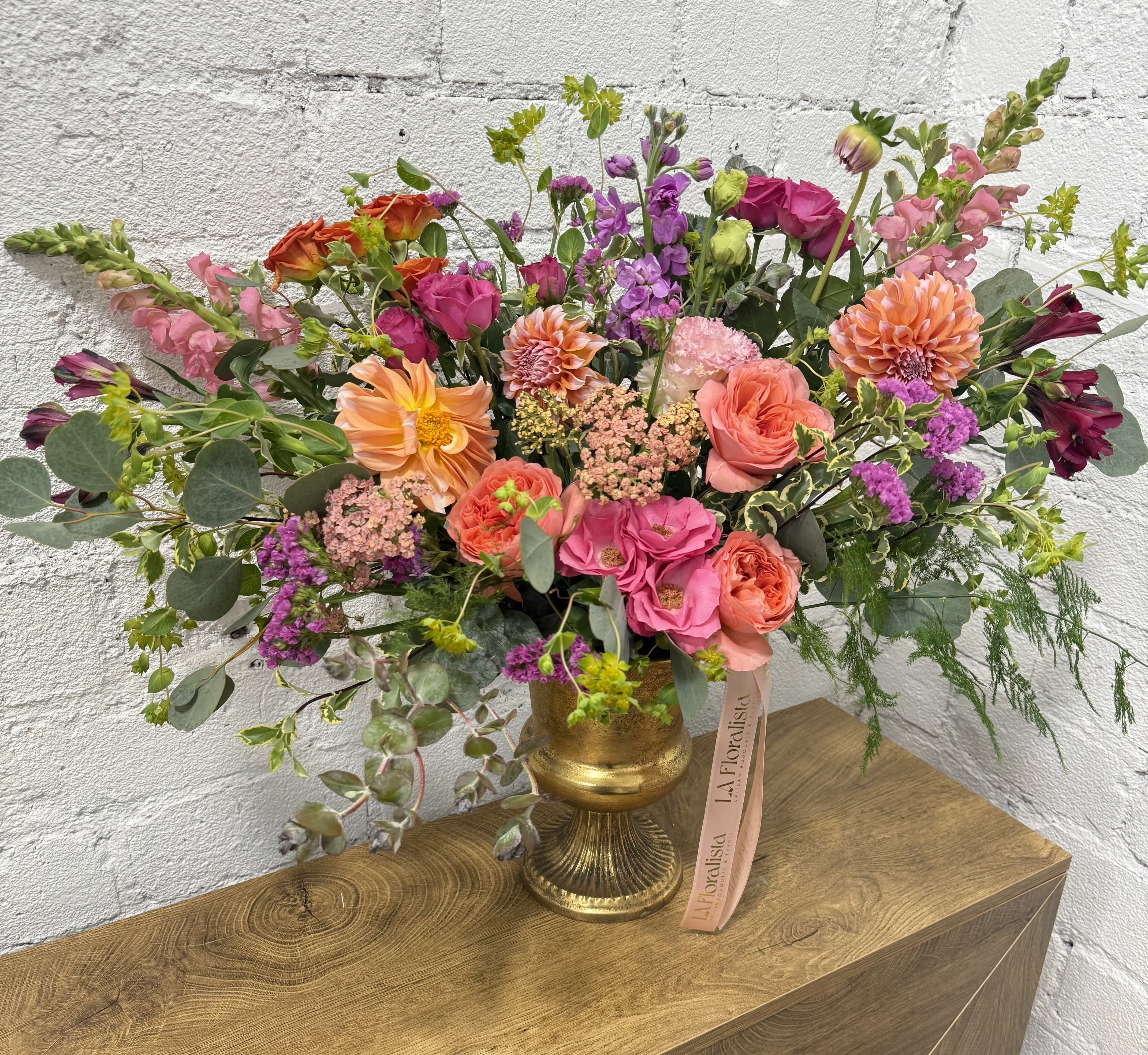 Large mixed bouquet in a gold vase with pink, orange, and purple flowers