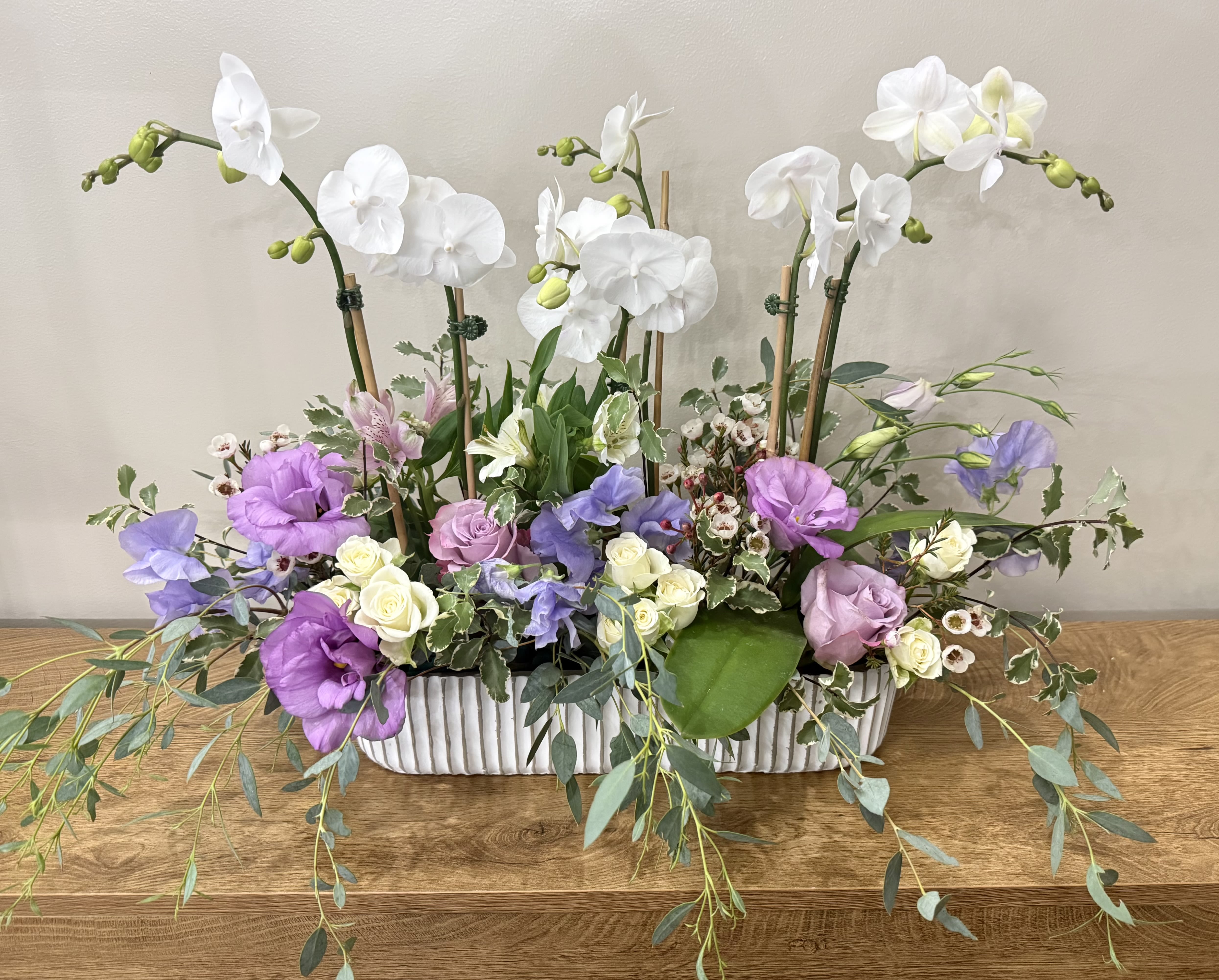 White orchids and purple flowers arranged in a rectangular vase