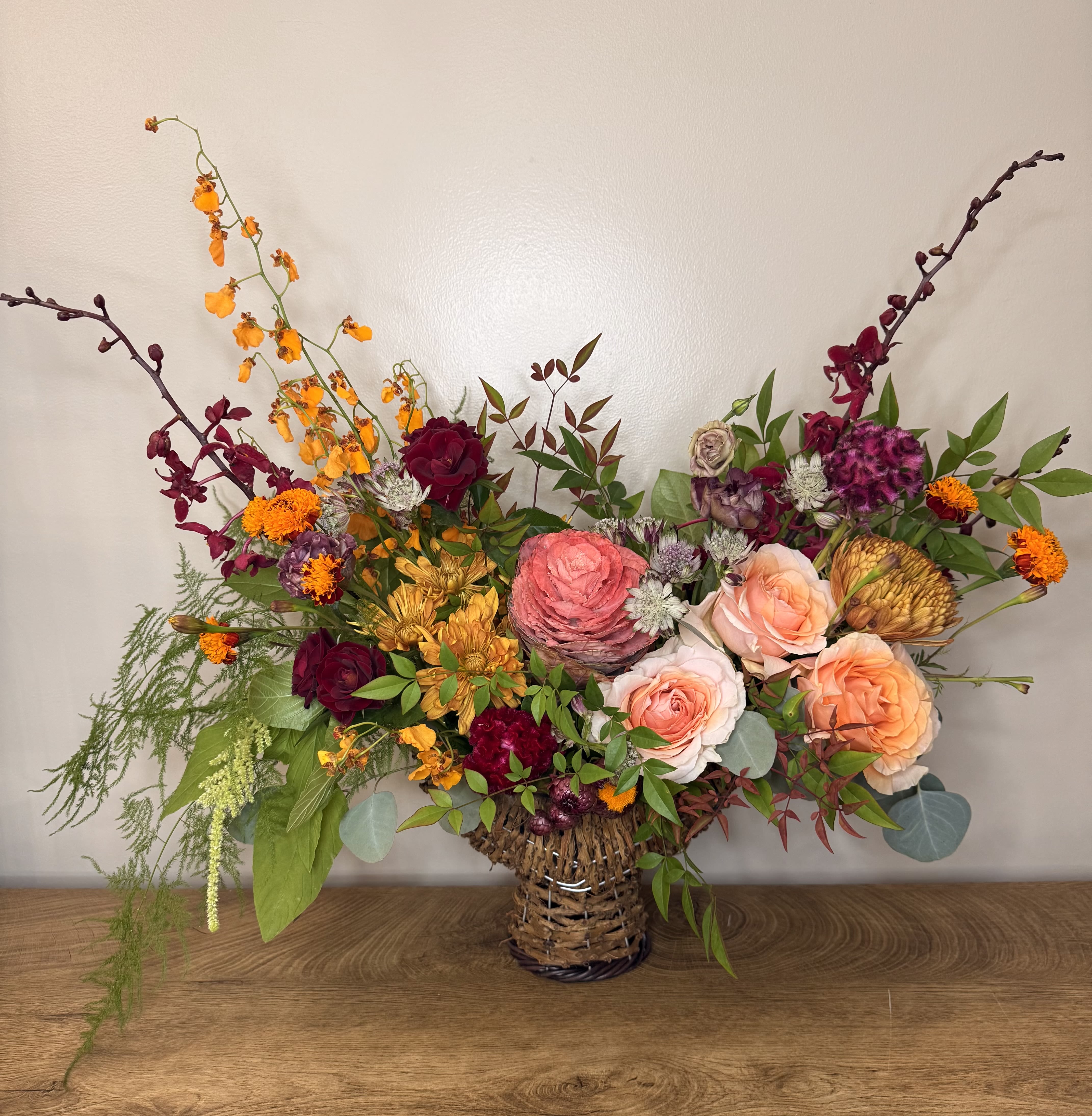 Mixed bouquet in a woven basket vase with roses and orange blooms