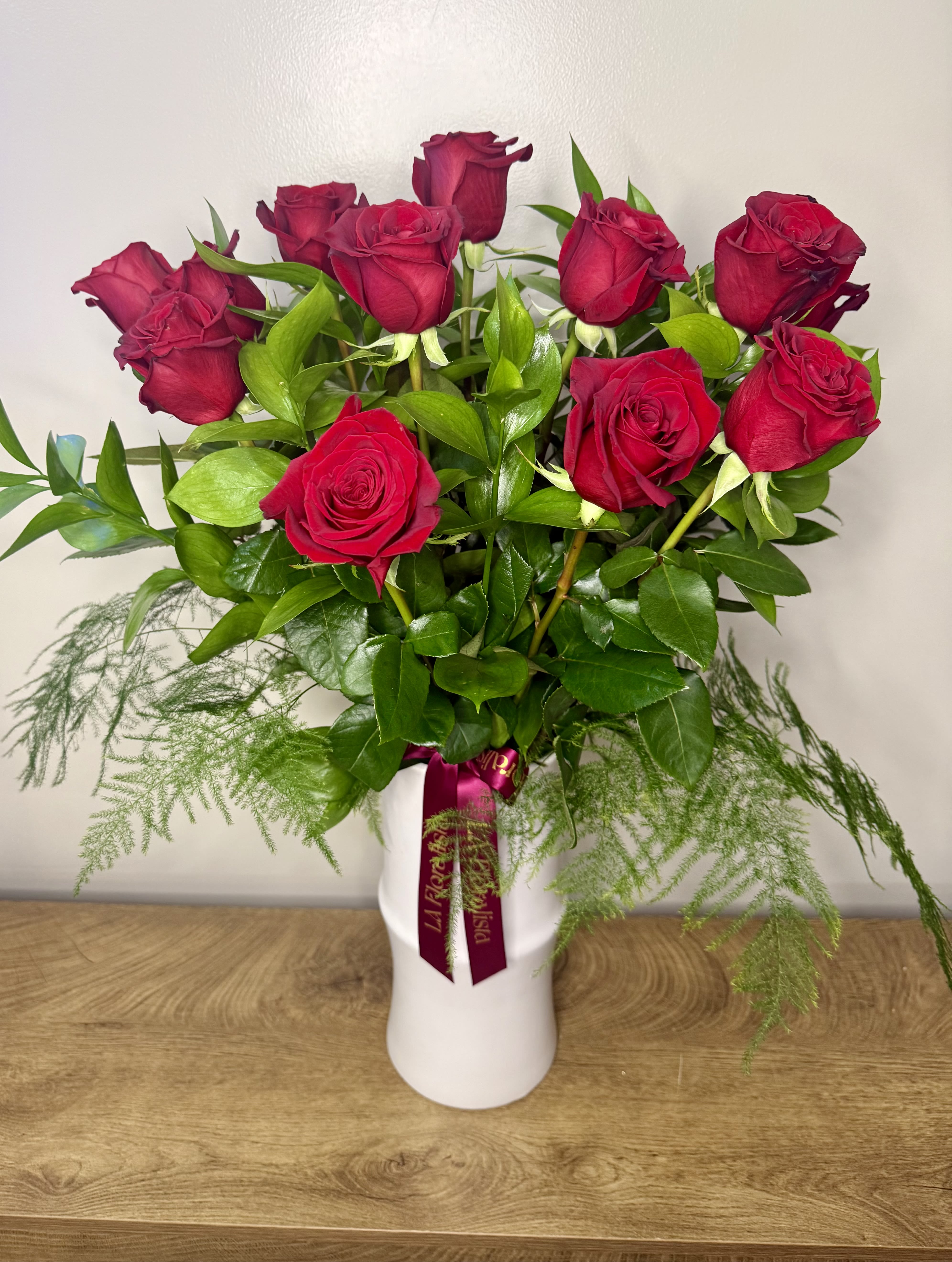 Red roses arranged in a white vase with trailing greenery.