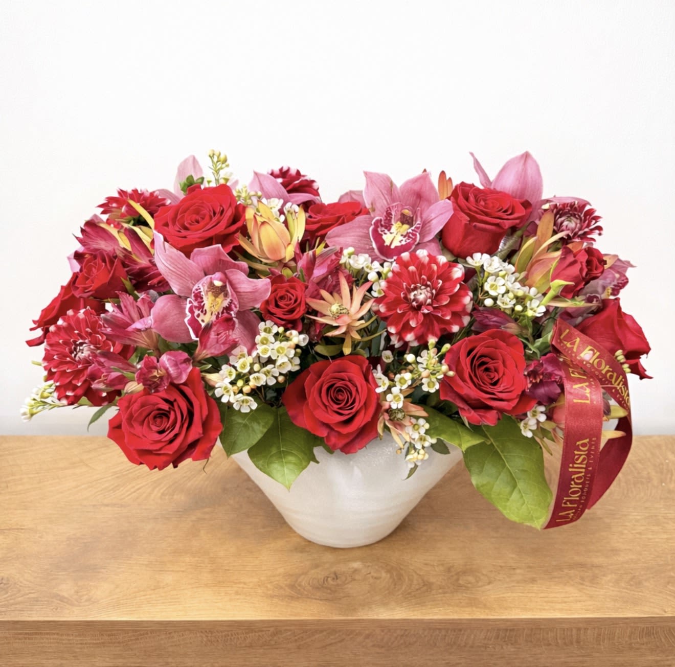 Red roses and pink orchids arranged in a white bowl vase