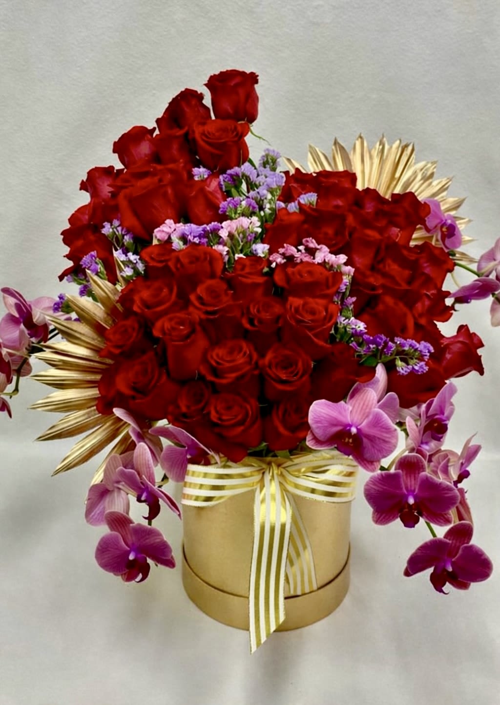 Red roses and purple orchids arranged in a gold box with ribbon