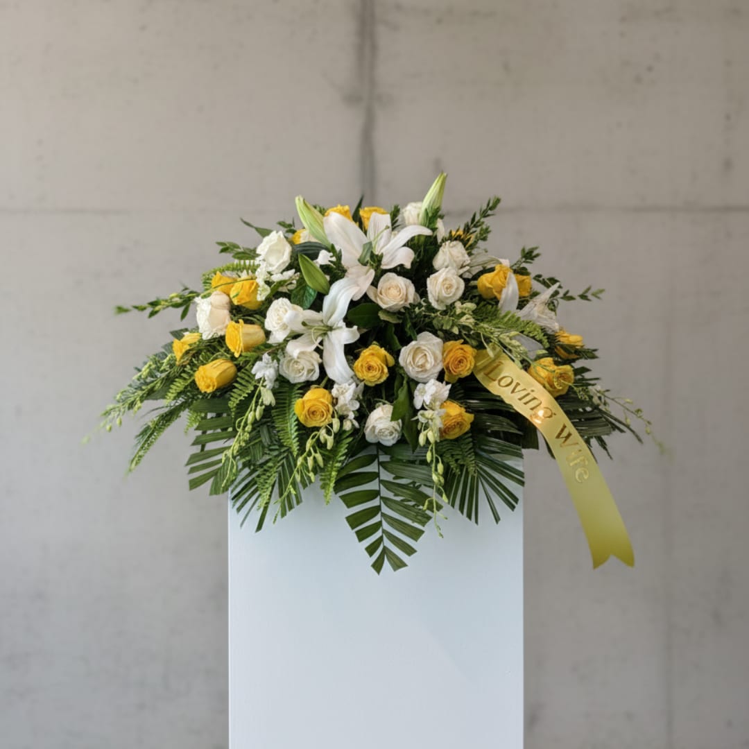 White and yellow floral arrangement on a pedestal with a ribbon