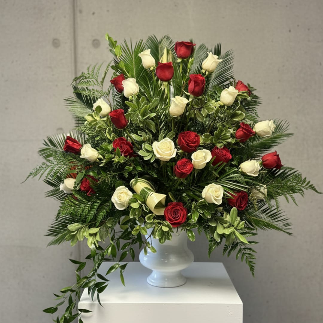 Red and white roses arranged in a white vase with lush greenery