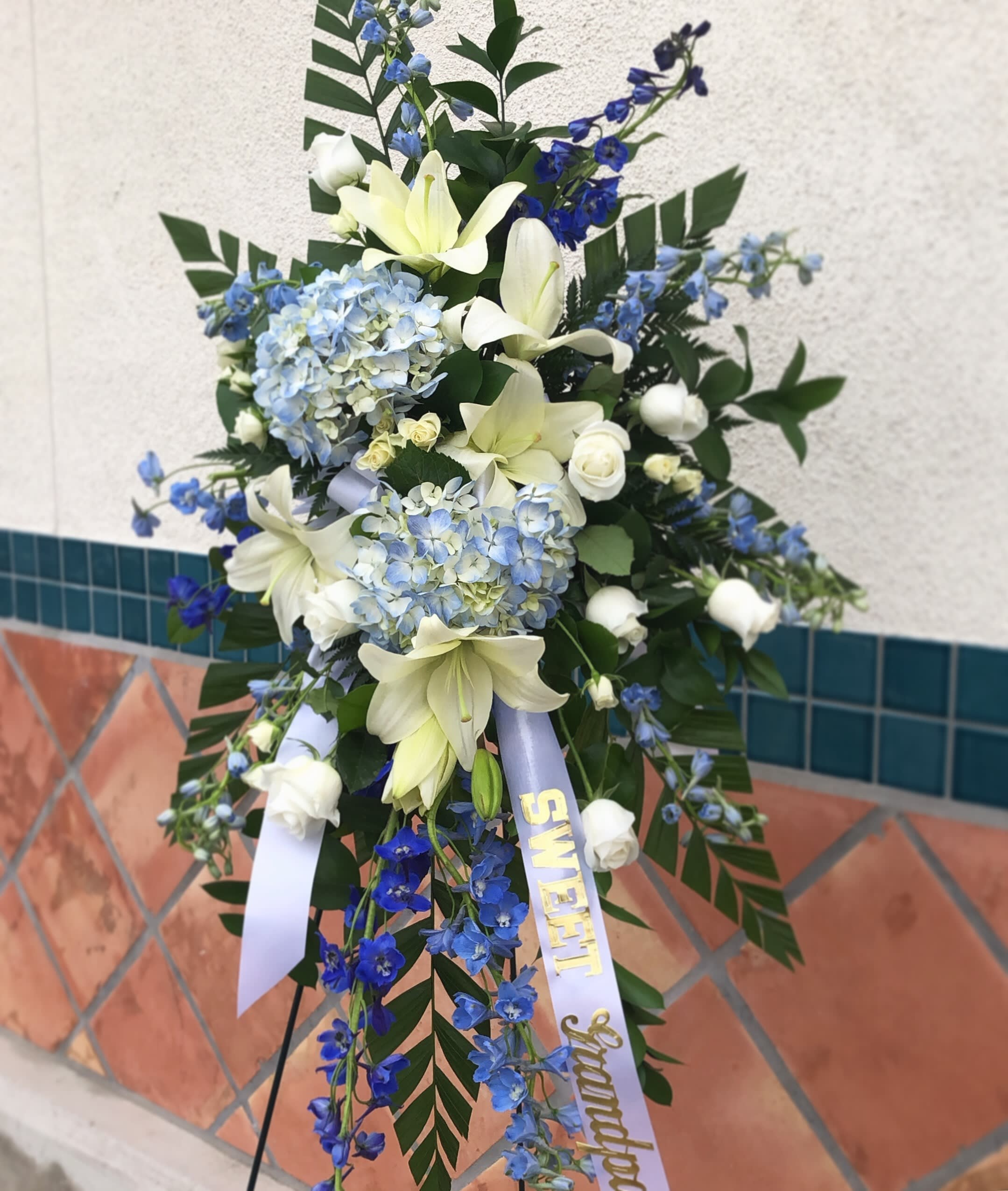 Standing floral spray with white lilies, blue hydrangeas, and blue delphinium