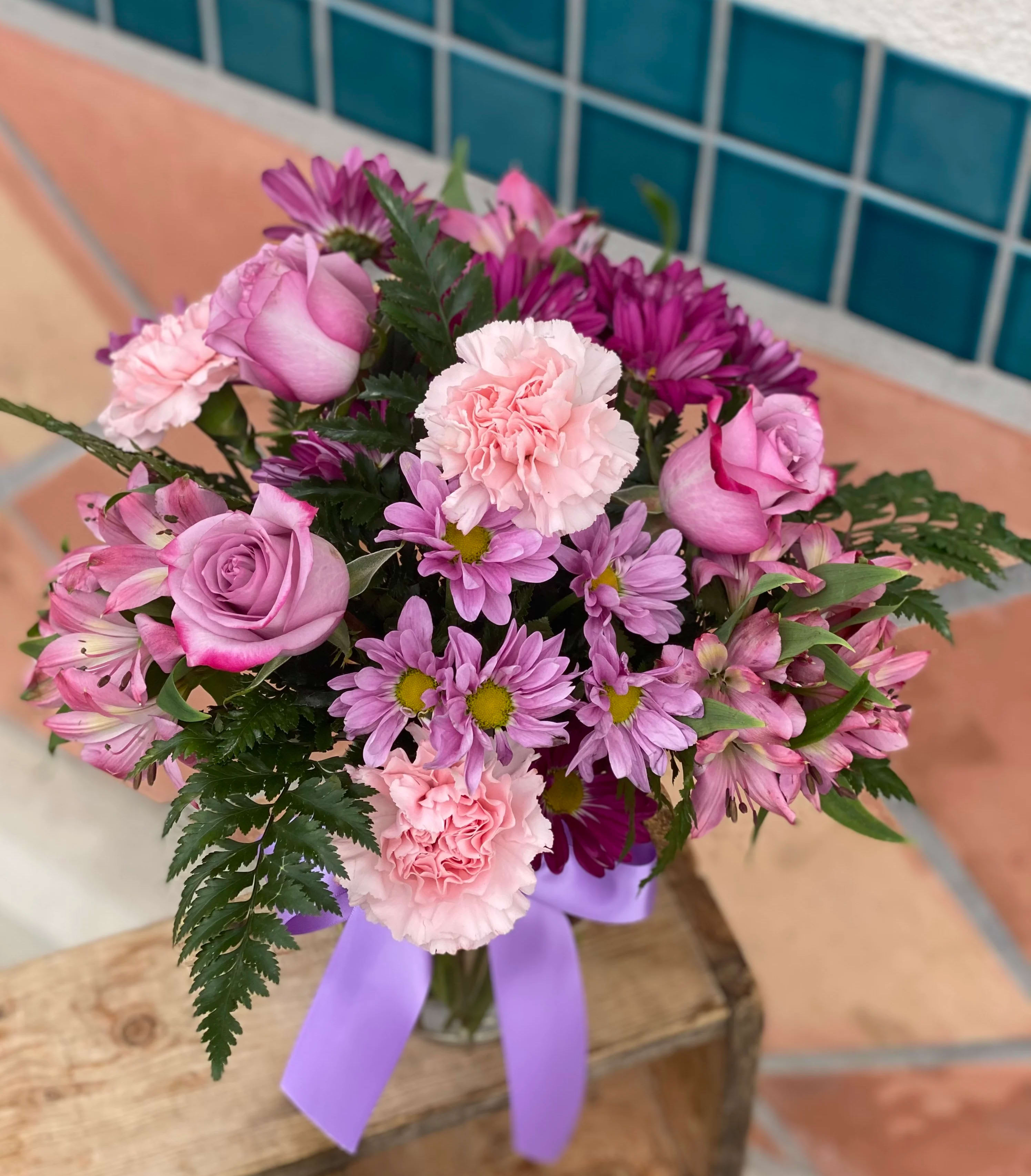Pink and purple bouquet in a glass vase with a lavender ribbon
