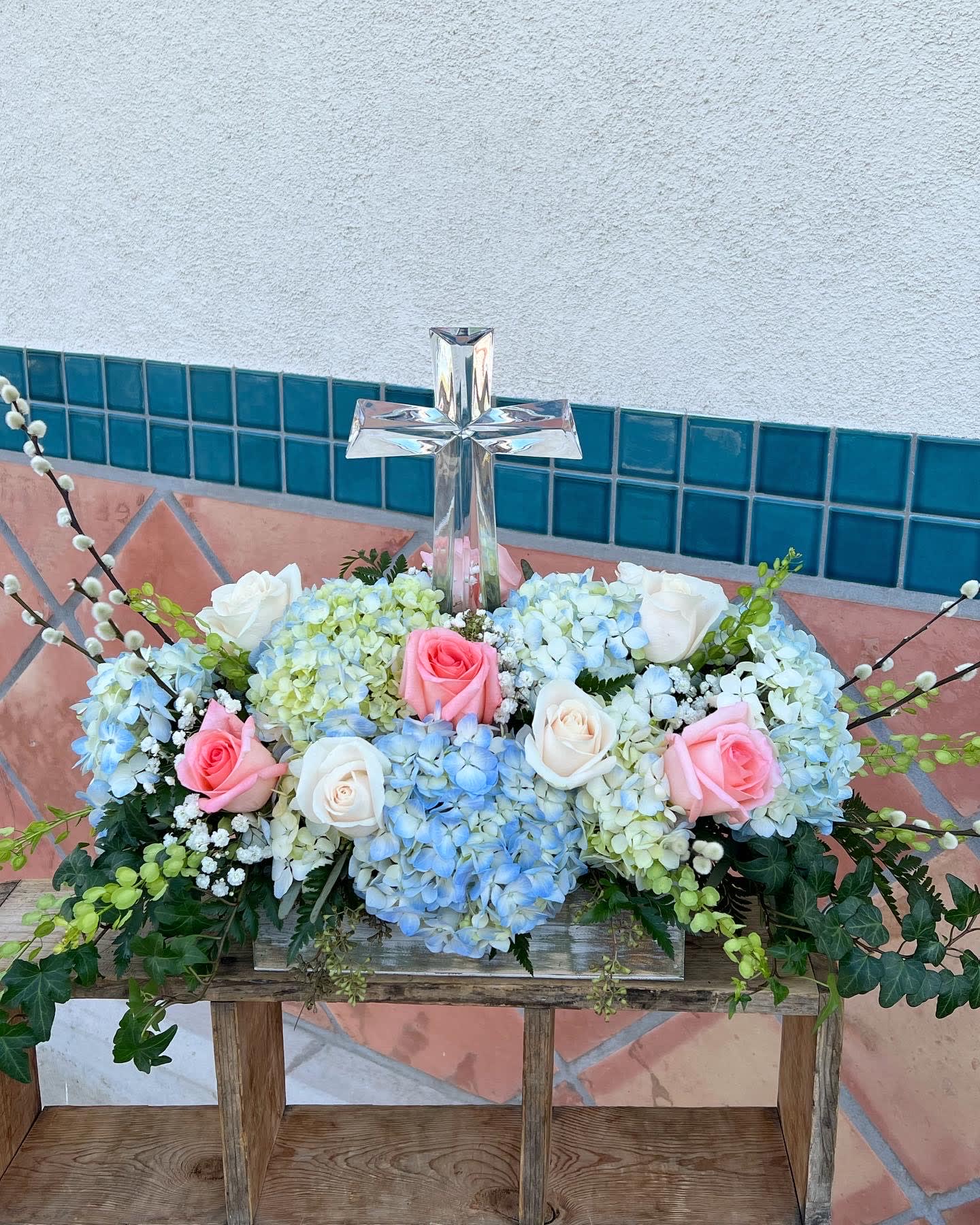 Floral arrangement with roses and hydrangeas around a clear glass cross