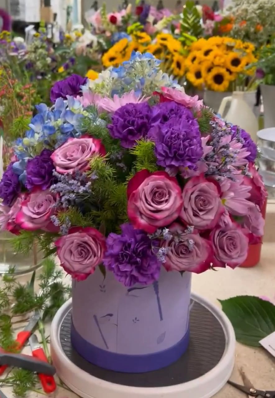 Round bouquet of pink and purple flowers in a lavender hat box