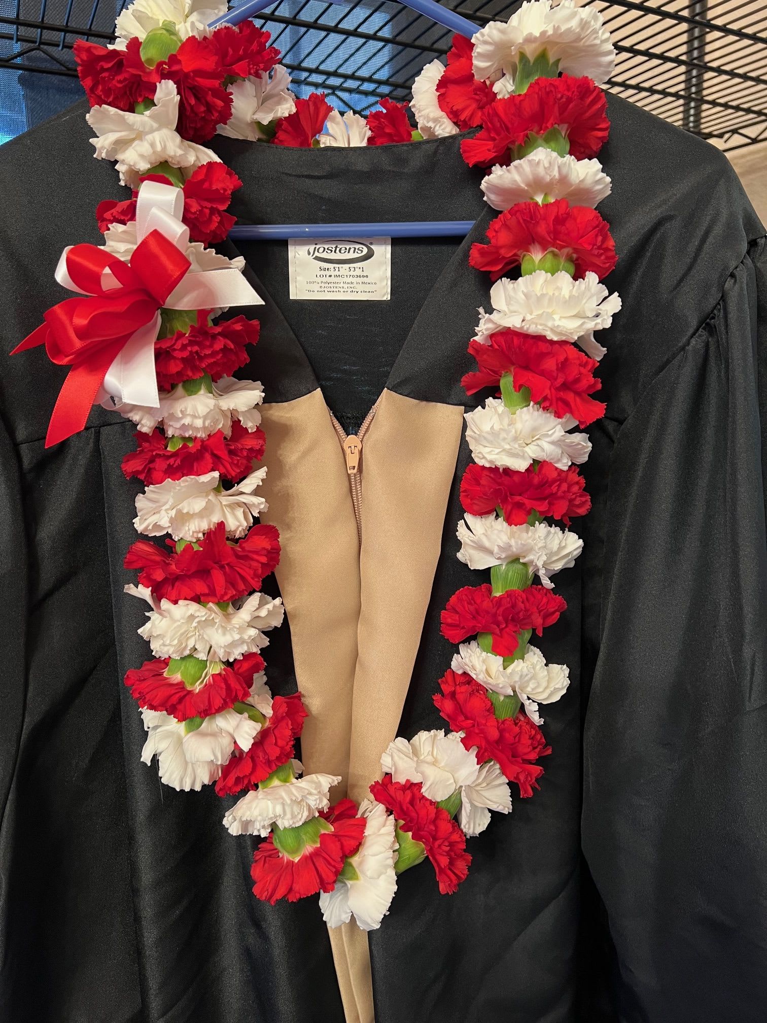 Red and white carnation lei draped over a black graduation gown