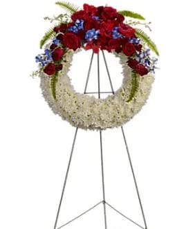 Circular funeral wreath of red and white flowers on a metal stand