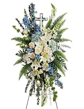 Standing funeral spray with white lilies, roses, and blue flowers on a cross easel