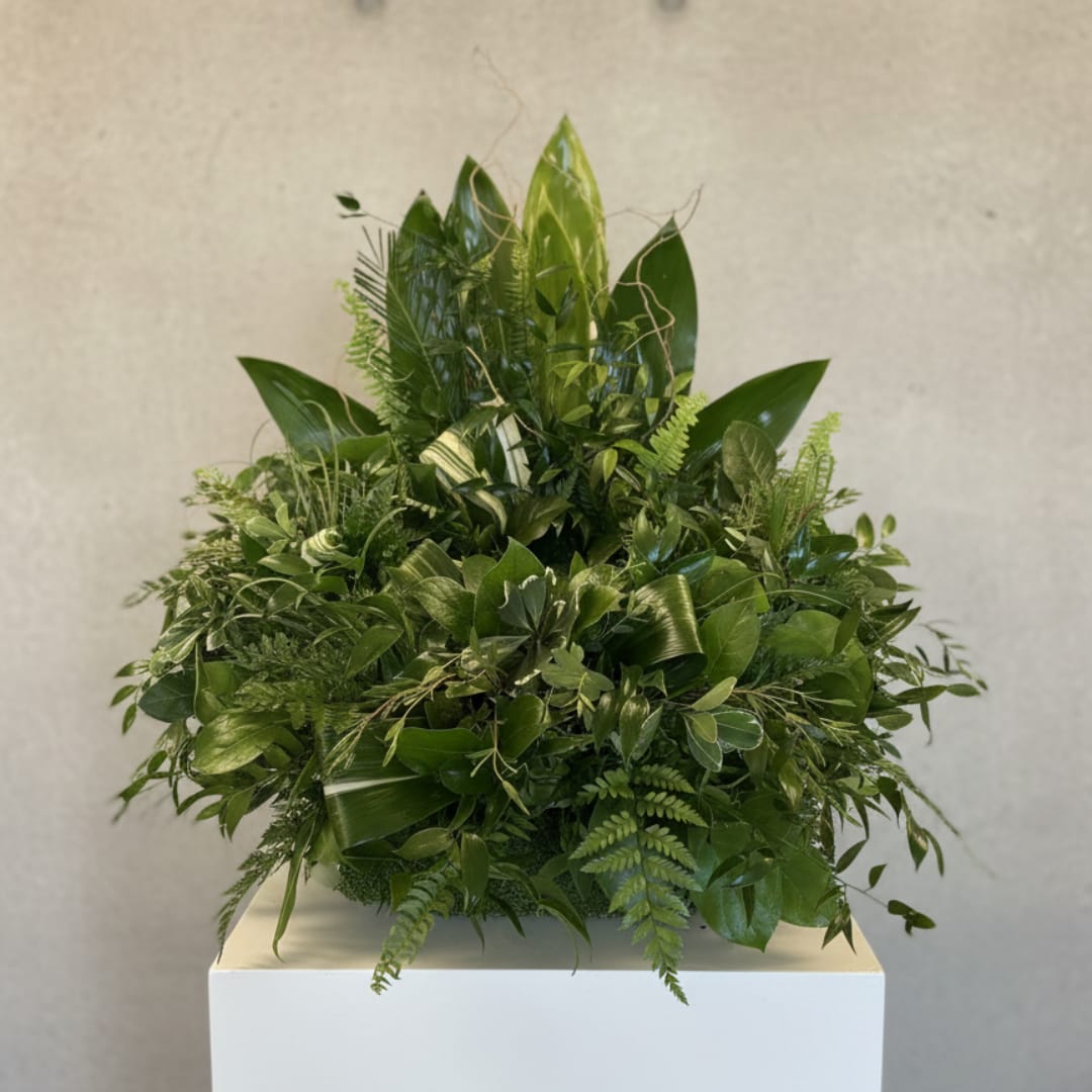 Dense green foliage arrangement on a white pedestal