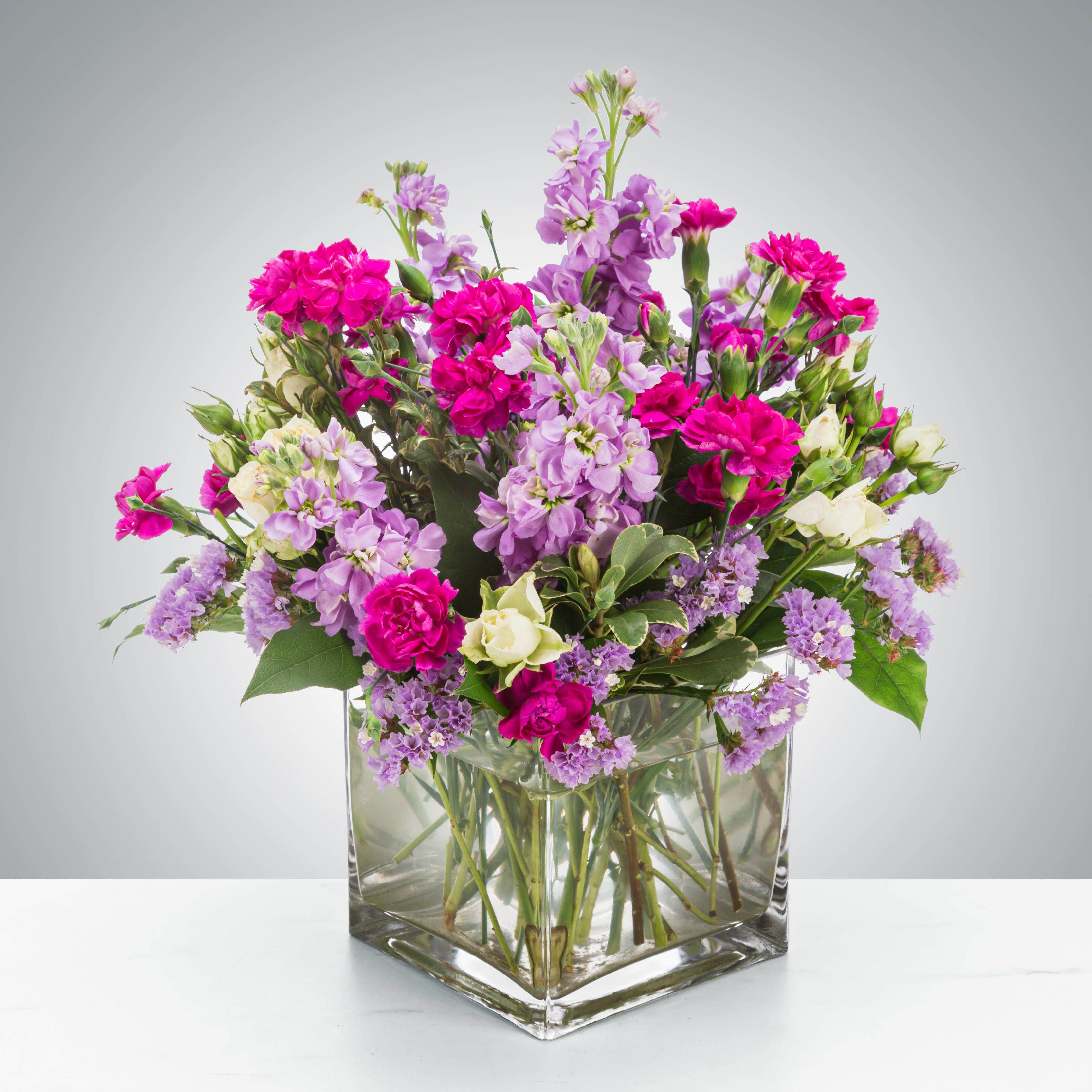 Pink and lavender flowers arranged in a clear square glass vase