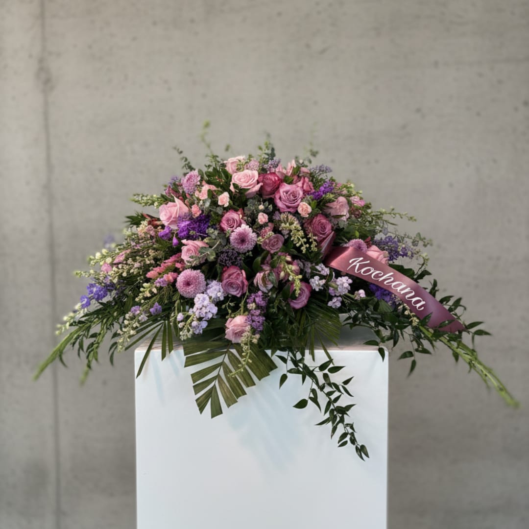 Pink and purple floral arrangement with a ribbon on a white pedestal