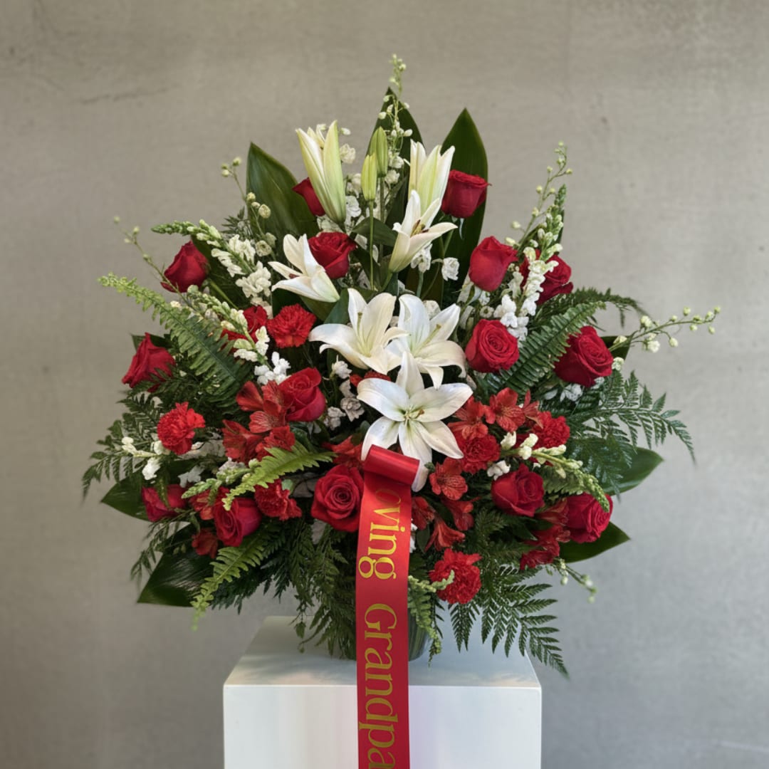 Red roses and white lilies arranged in a vase with a red ribbon
